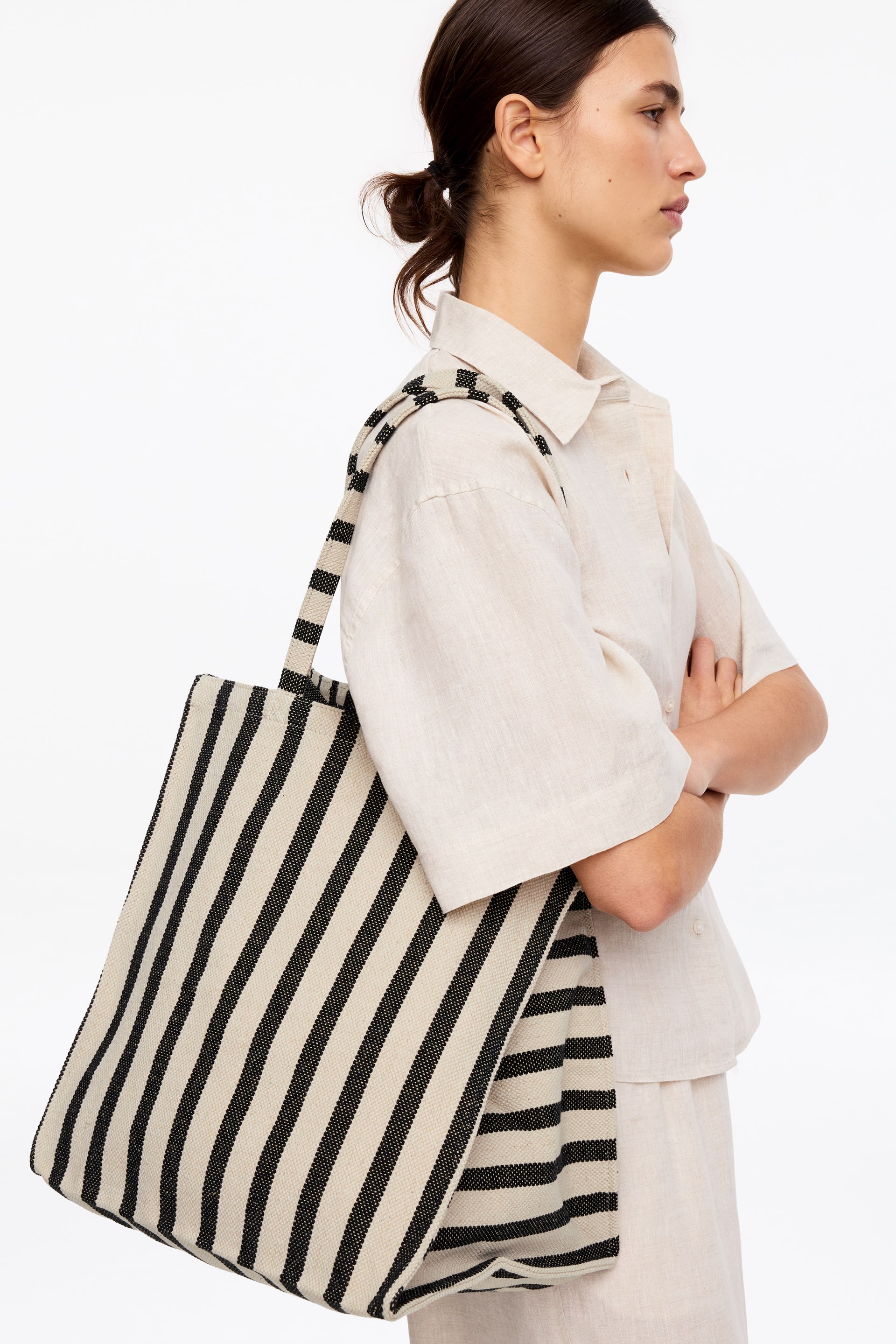 Se større billede: En vævet tote taske viser lodrette sorte og off-white striber, med hoveddelen let fremad og til venstre. Den hænger fra en skulder, og dens rem har også det matchende stribede mønster.