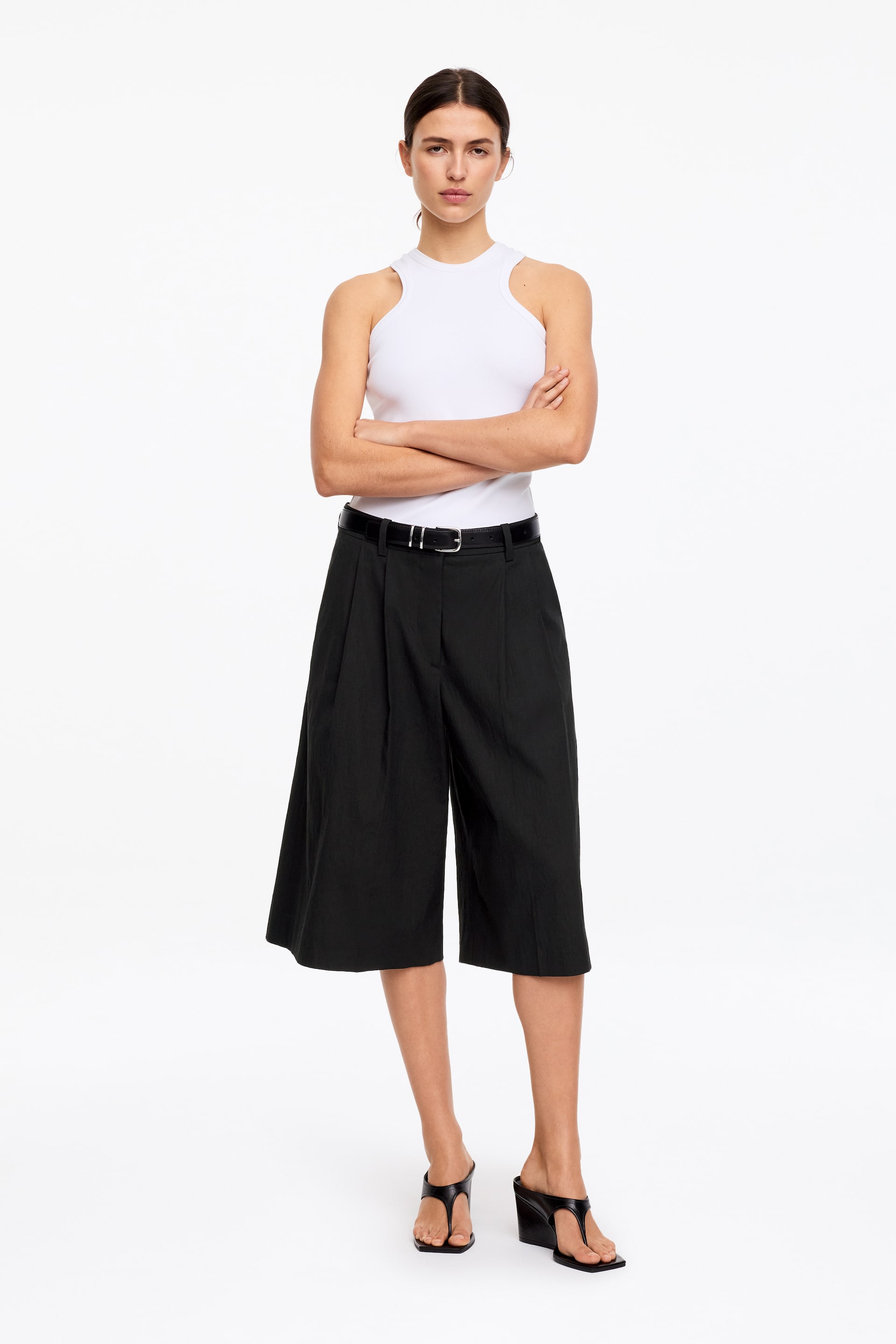 Visa större bild: Svarta vida culottes med hög midja, framhäver frontveck och ett texturerat tyg, presenterade framifrån. Ett svart bälte med ett silverfärgat spänne markerar midjan, och culottes når till mitten av vaden.