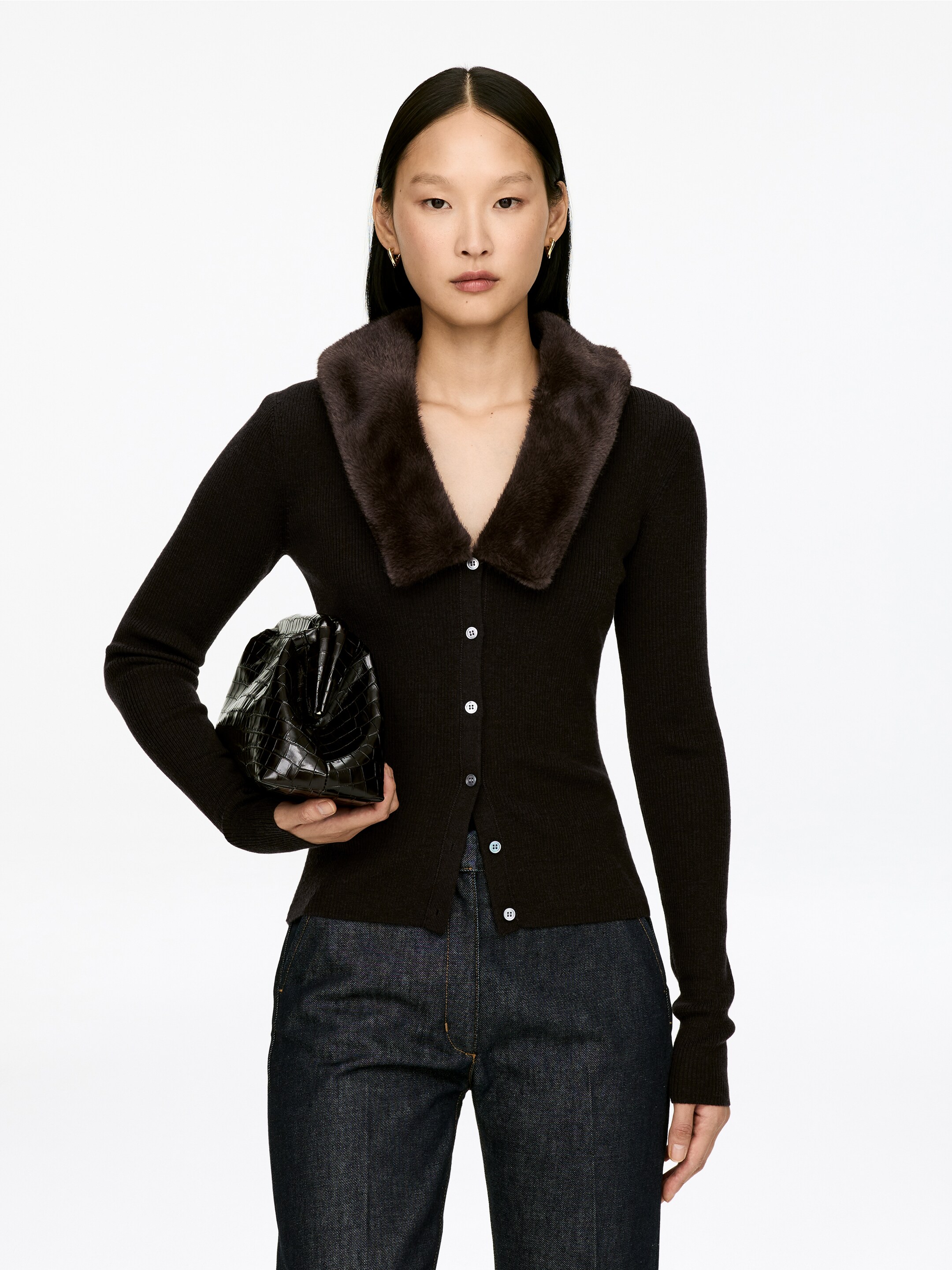Agrandir l'image: Un cardigan en maille côtelée marron foncé est montré de face, avec un large col en fausse fourrure de la même teinte marron foncé. Il est conçu avec une fermeture à boutons sur le devant, accentuée par des boutons ronds de couleur claire, et des manches longues avec une silhouette ajustée.
