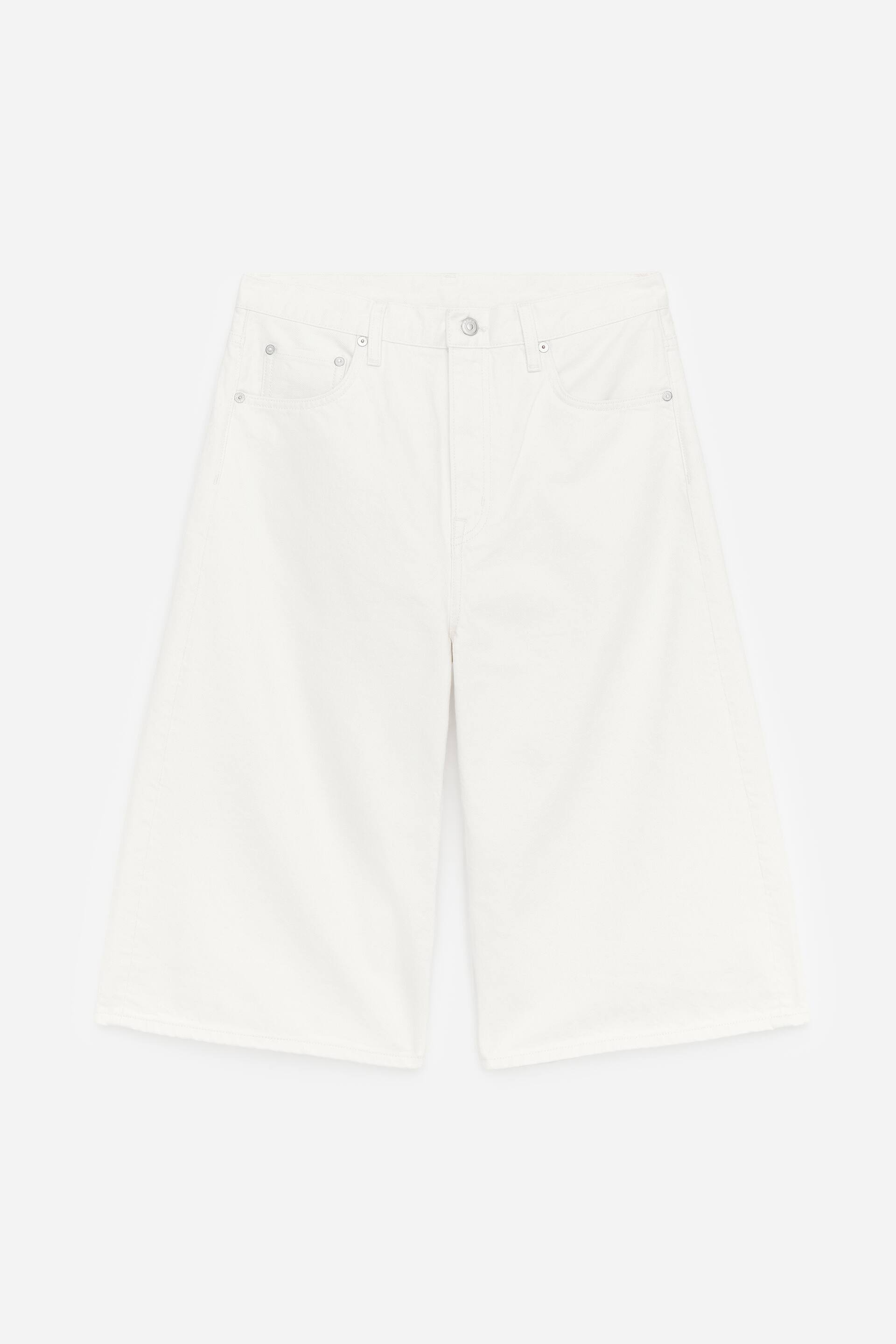 Visualizza immagine più grande: I bermuda in denim bianco lungo sono presentati frontalmente, caratterizzati da una silhouette rilassata e un taglio al ginocchio. Sono progettati con una classica costruzione a cinque tasche, una chiusura con zip e un bottone a pressione in metallo.