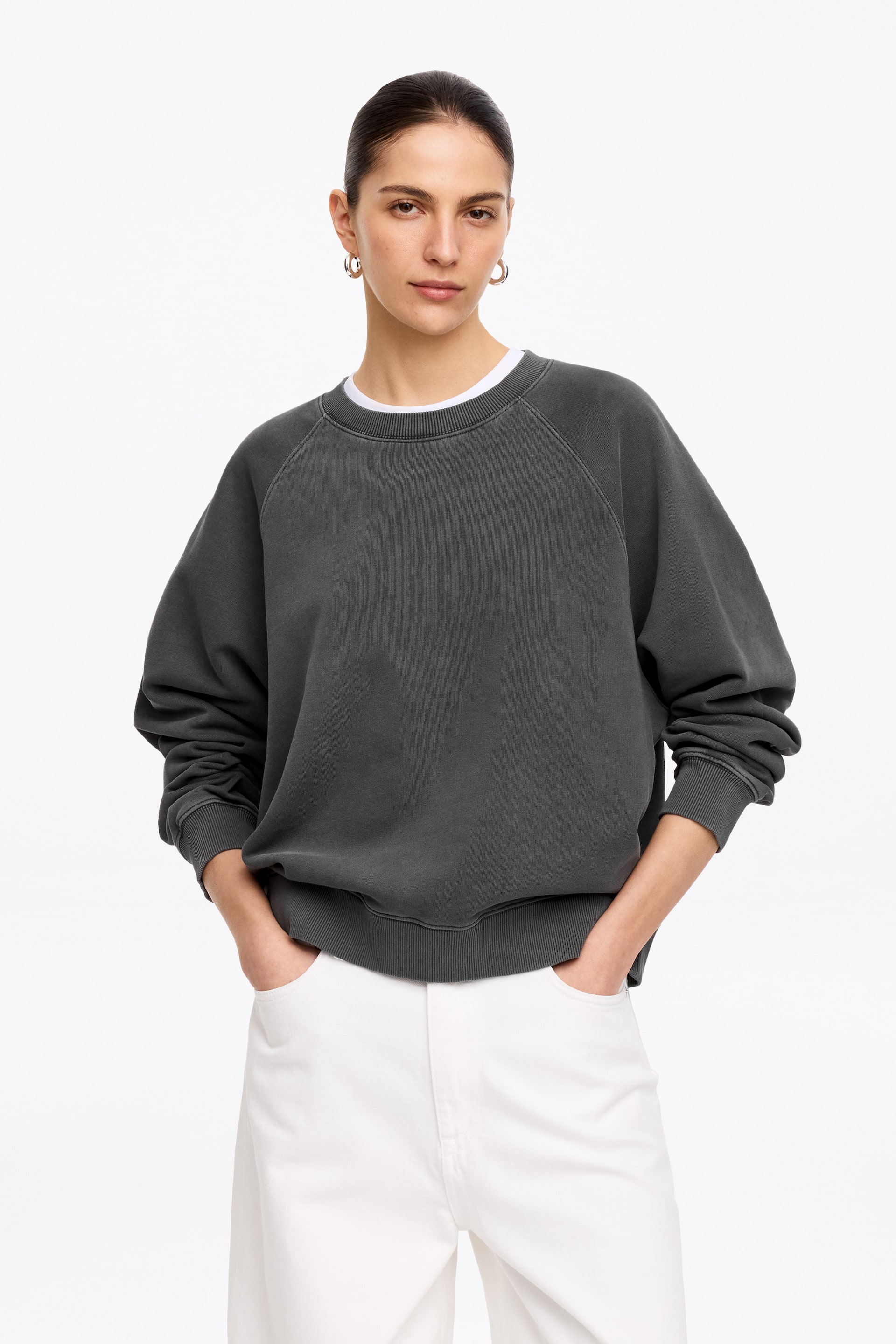 Visa större bild: Den mörkgrå sweatshirten har en rund hals, raglanärmar, ribbade muddar och en ribbad fåll. Den presenteras framifrån, med en vit t-shirt synlig vid halsringningen.