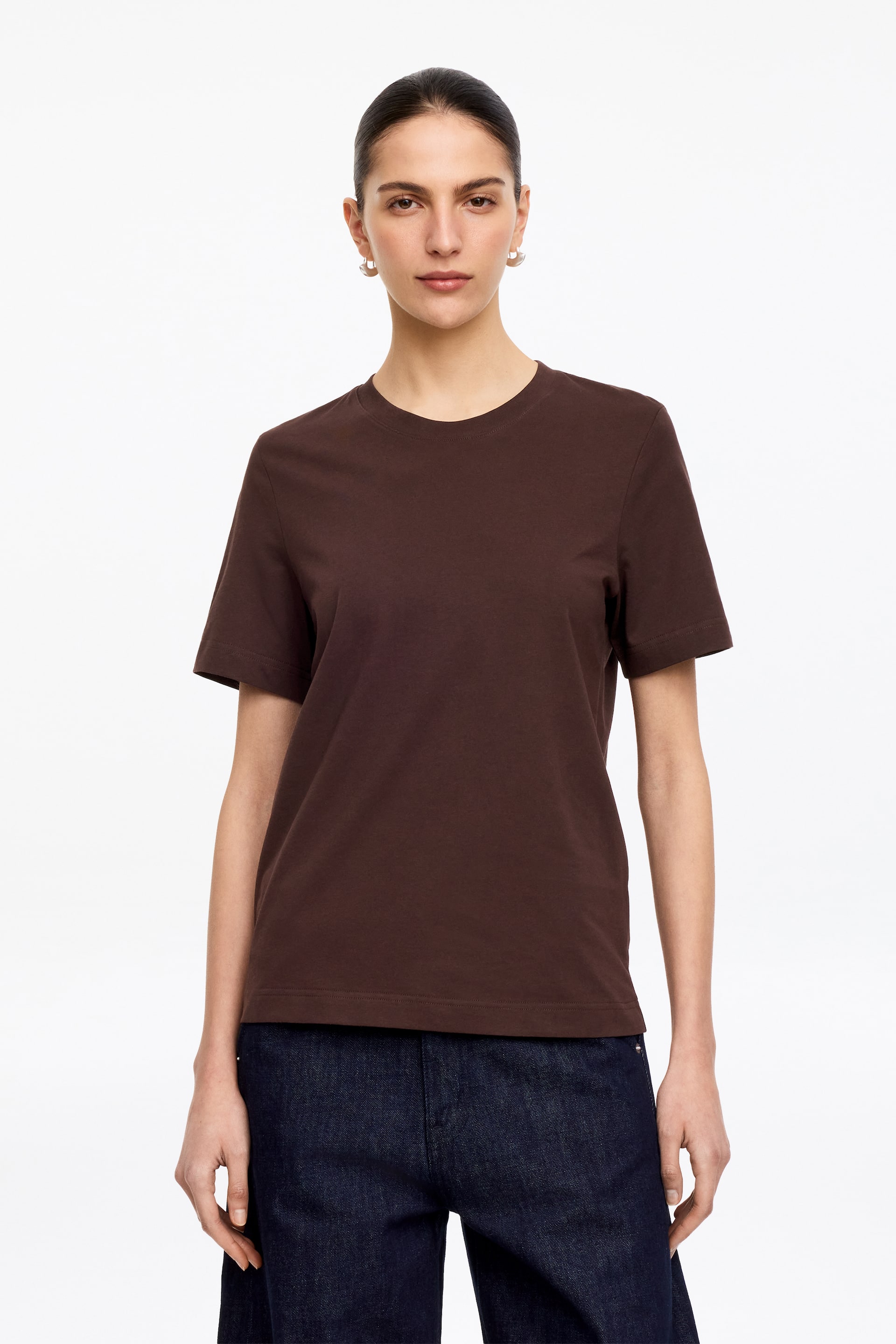 Ver imagem maior: Uma t-shirt lisa de cor castanho escuro é apresentada de frente, com decote redondo, mangas curtas e bainha reta.