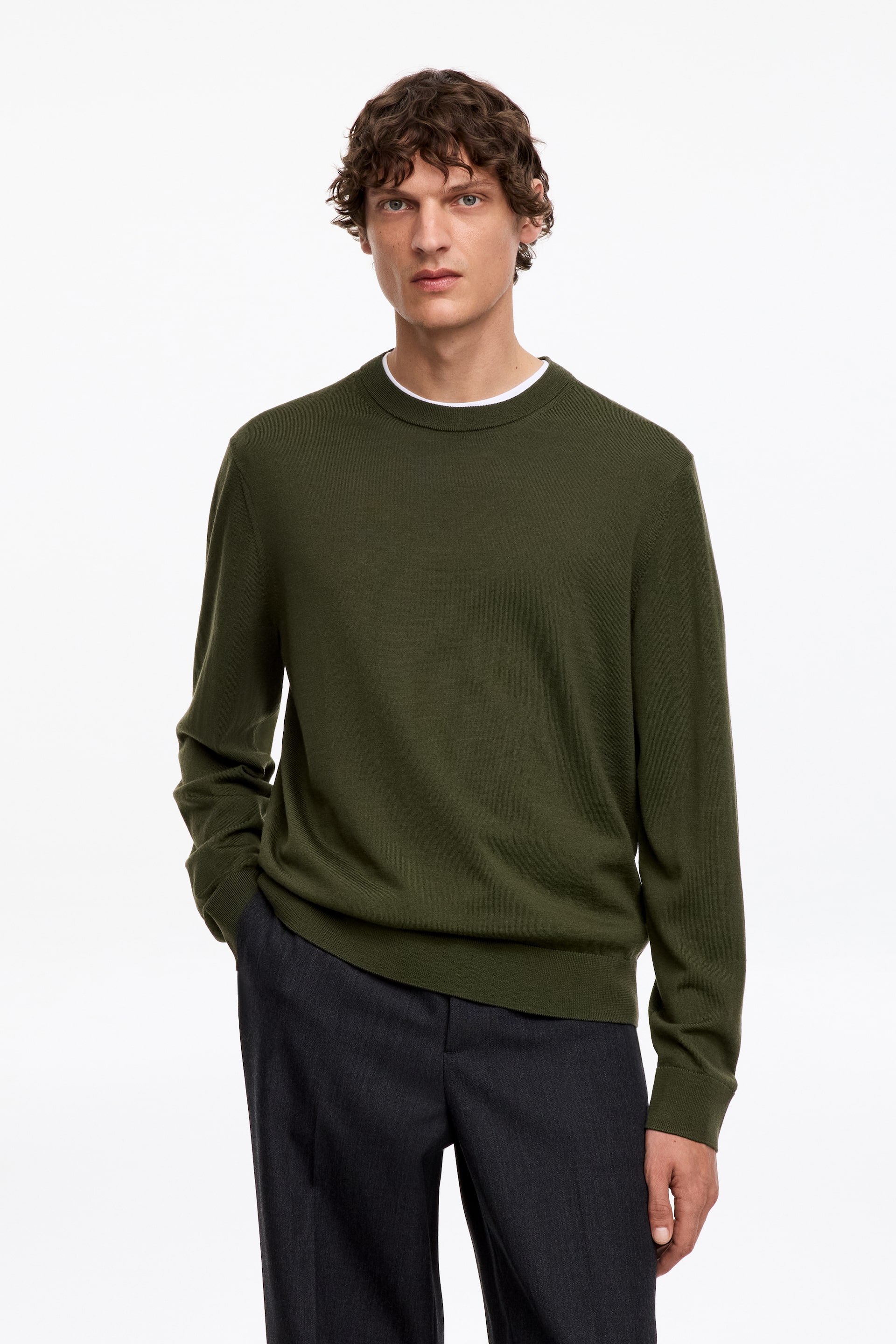 Ver imagen más grande: La modelo lleva un jersey verde de punto fino con cuello redondo. Presenta detalles acanalados en el cuello, los puños y el dobladillo, y está superpuesto sobre una camiseta blanca.