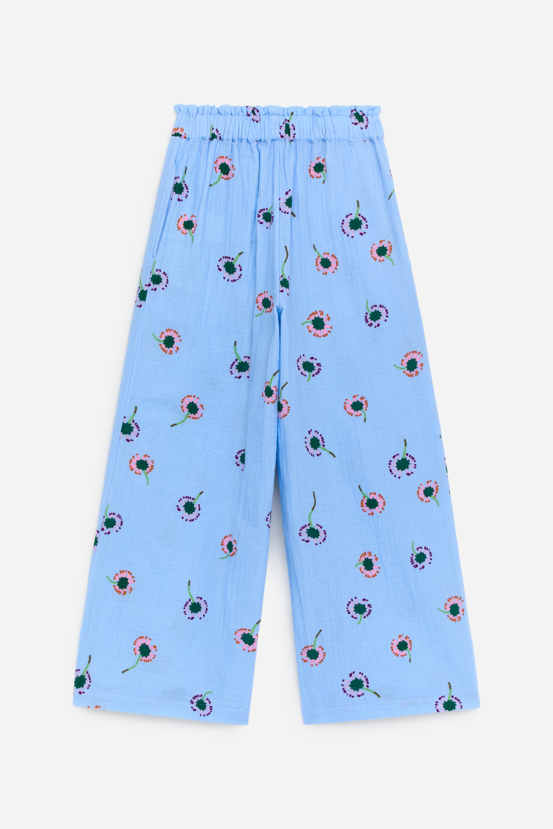Größeres Bild ansehen: Die Hose präsentiert sich in einem hellblauen, geknitterten Stoff und zeigt ein verstreutes Blumenmuster mit rosa, lila und grünen Elementen. Sie ist mit einem gesmokten elastischen Bund, sichtbaren Seitentaschen und einer weiten, verkürzten Silhouette gestaltet.