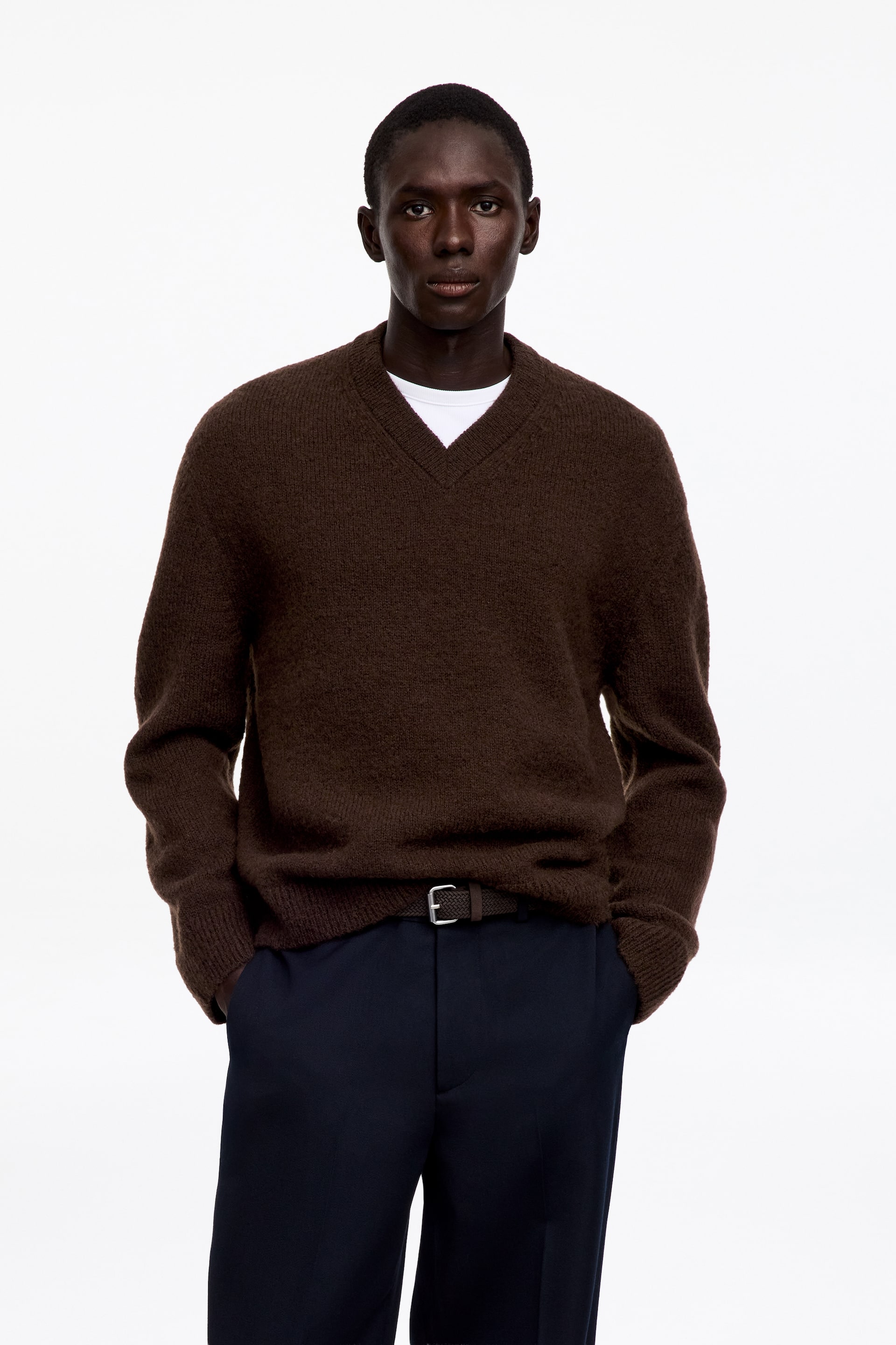 Se større billede: En brun V-hals sweater med en tekstureret strikstruktur bæres af modellen. Den er lagt i lag over en hvid T-shirt med rund hals.