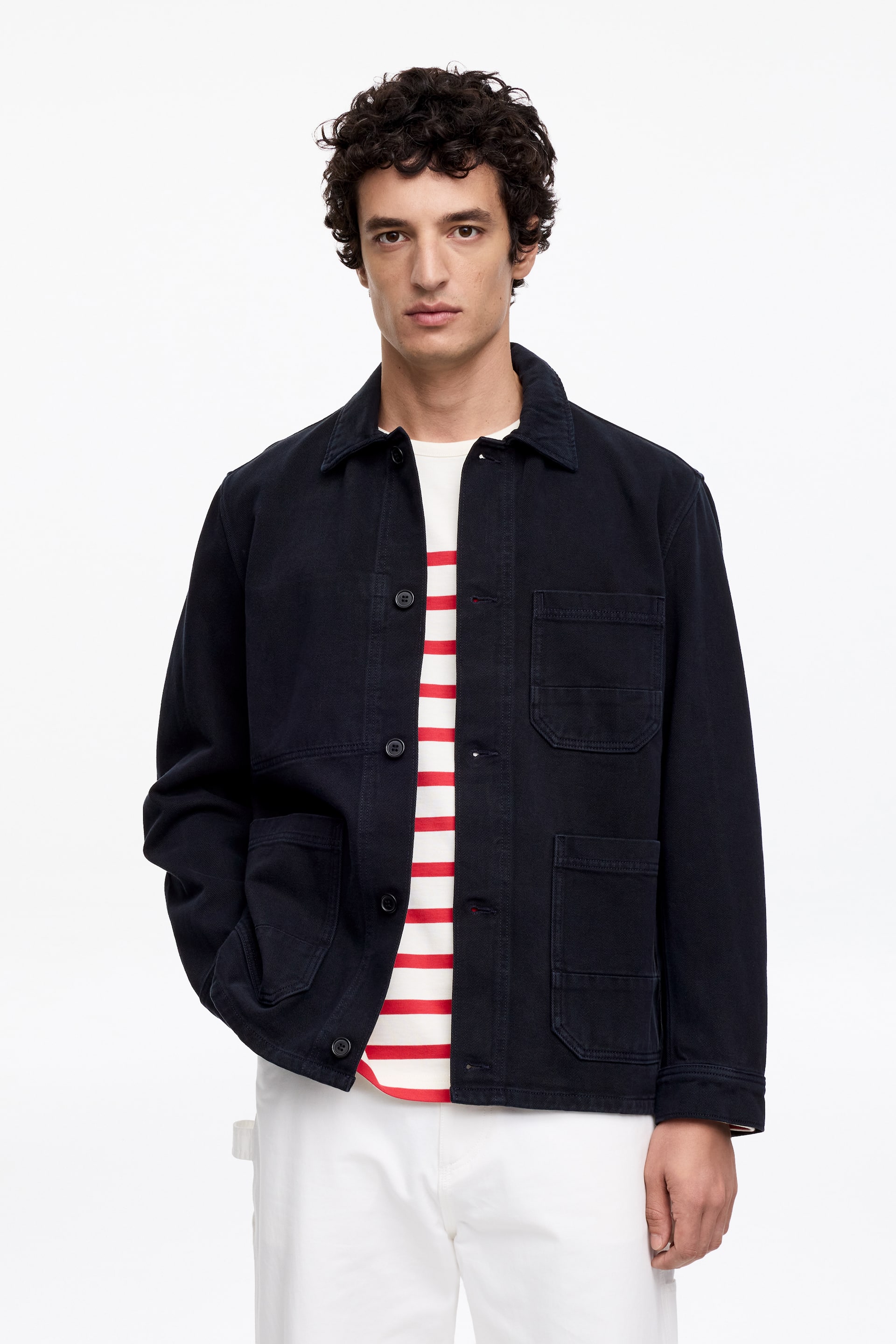 Visa större bild: En mörkblå jacka med spetsig krage, knappstängning framtill med mörka knappar och långa ärmar med knappförsedda manschetter. Den har två bröstfickor med lock, två stora nedre fickor och en extra liten ficka på nedre högra sidan, bärs öppen över en vit och röd randig t-shirt.
