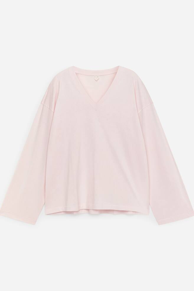 En ljusrosa, löst sittande långärmad T-shirt visar sin framsida, med en ribbad V-ringning och vida ärmar som avslutas i raka fållar. - 1