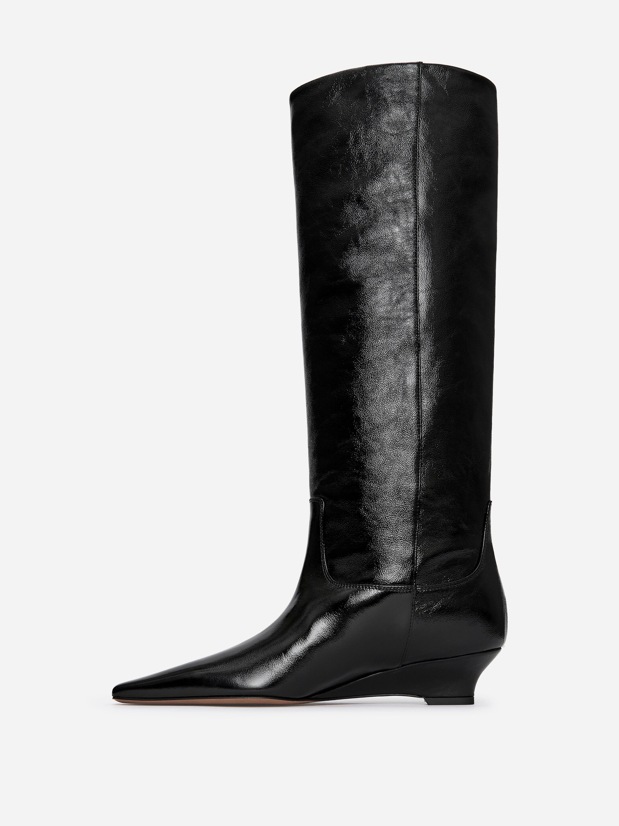Agrandir l'image: Une botte noire haute est orientée vers la droite, avec un bout pointu et un talon compensé bas. Le pied de la botte est fabriqué en cuir lisse et brillant, tandis que la tige haute présente une texture froissée distincte.
