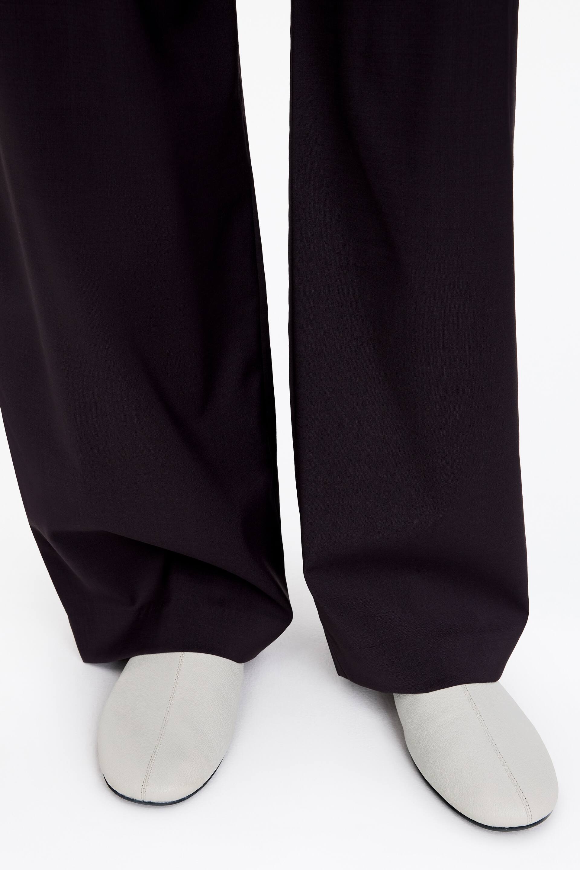 Vis større bilde: Mørke bukser med vide ben faller rett over lysegrå lærsko med rund tå og en synlig midtsøm.