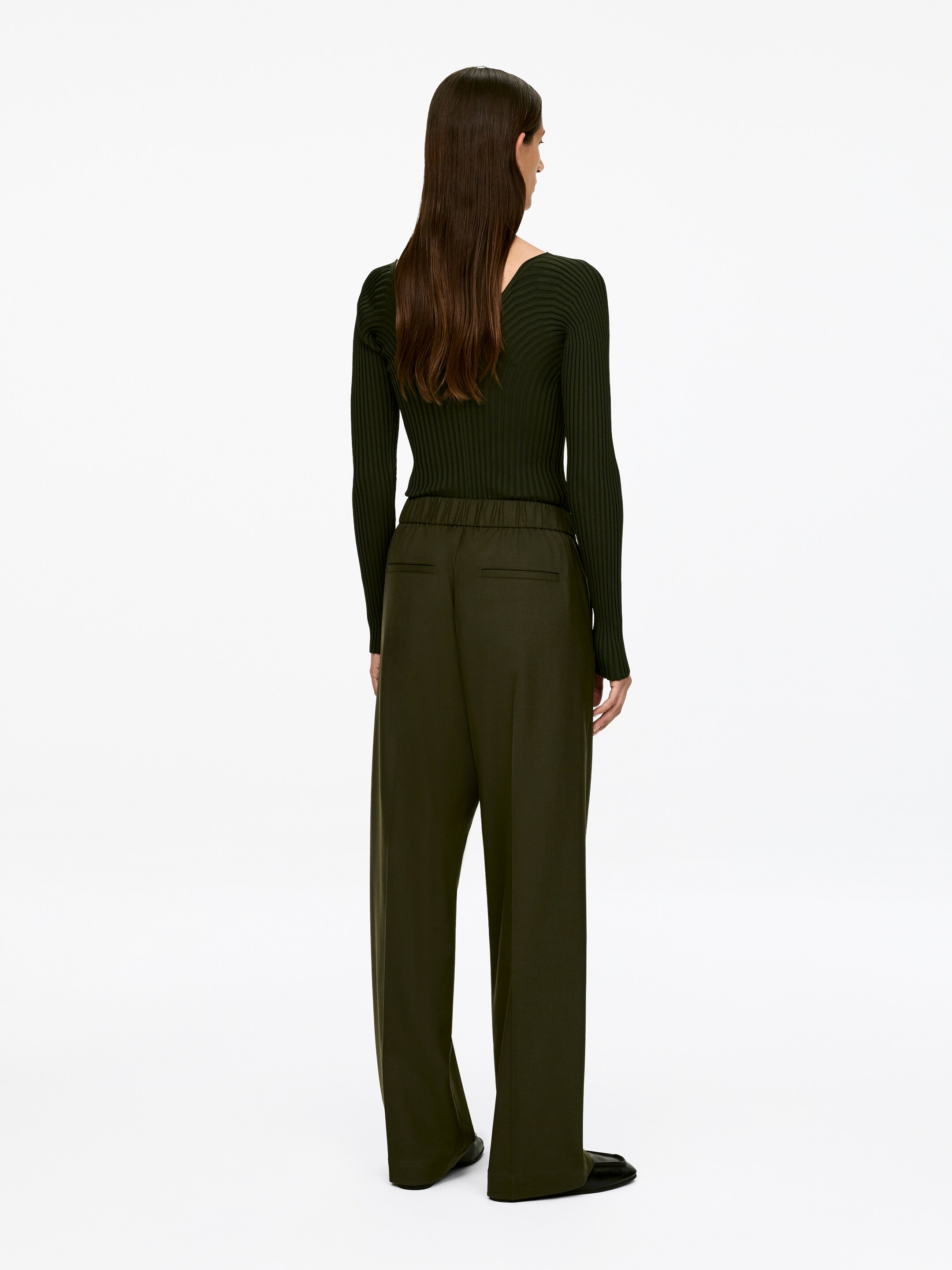 View larger image: A dark green ribbed long-sleeved top and dark olive green wide-leg trousers are being shown, presented from the back. The top is displaying a V-neckline at the back, and the trousers are featuring an elasticated waistband and back welt pockets.