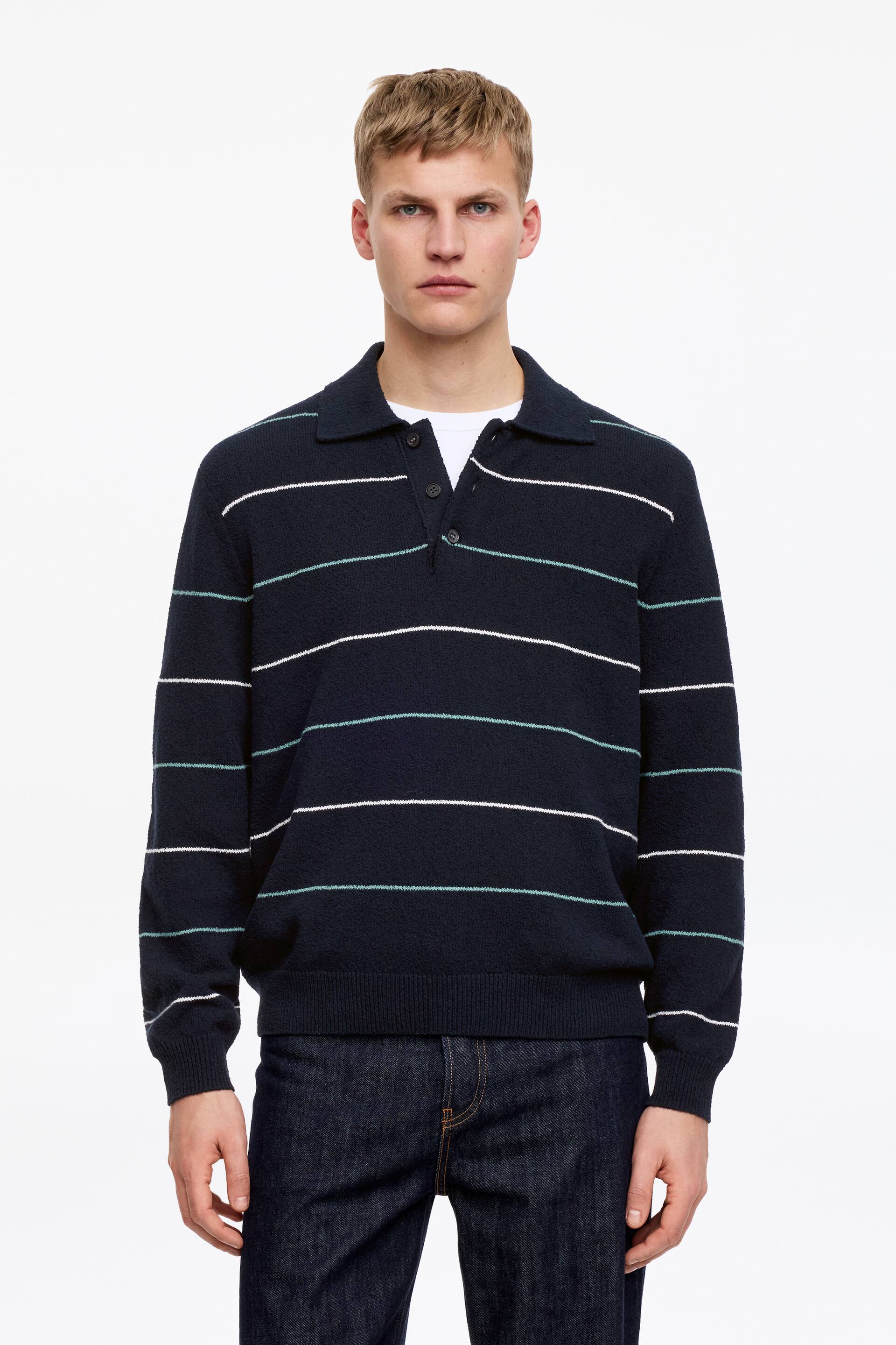 Vezi imaginea mai mare: Un pulover pentru bărbați, de culoare albastru închis, prezintă dungi orizontale albe și verde mentă, un guler polo cu o deschidere cu două nasturi și manșete și tivuri cu nervuri. Un tricou alb este vizibil sub gulerul descheiat, iar puloverul este prezentat cu fața în față.