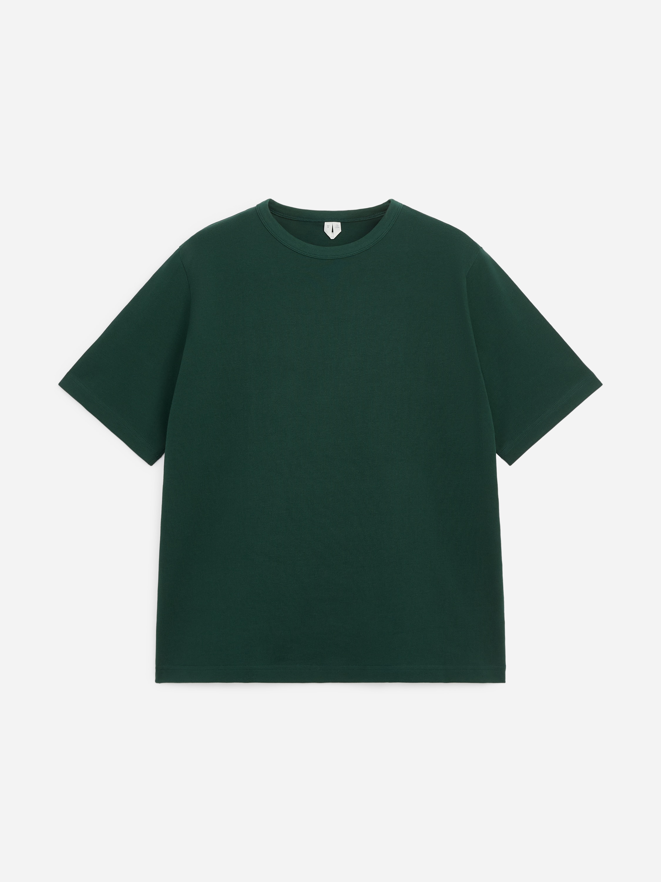 En mÃ¸rkegrÃ¸n T-shirt med rund hals og kraftig kvalitet bÃ¦res af modellen og har en afslappet pasform, en ribstrikket halsudskÃ¦ring og lidt lÃ¦ngere korte Ã¦rmer. Modellen stÃ¥r med den ene hÃ¥nd hvilende i lommen pÃ¥ mÃ¸rkeblÃ¥ jeans.