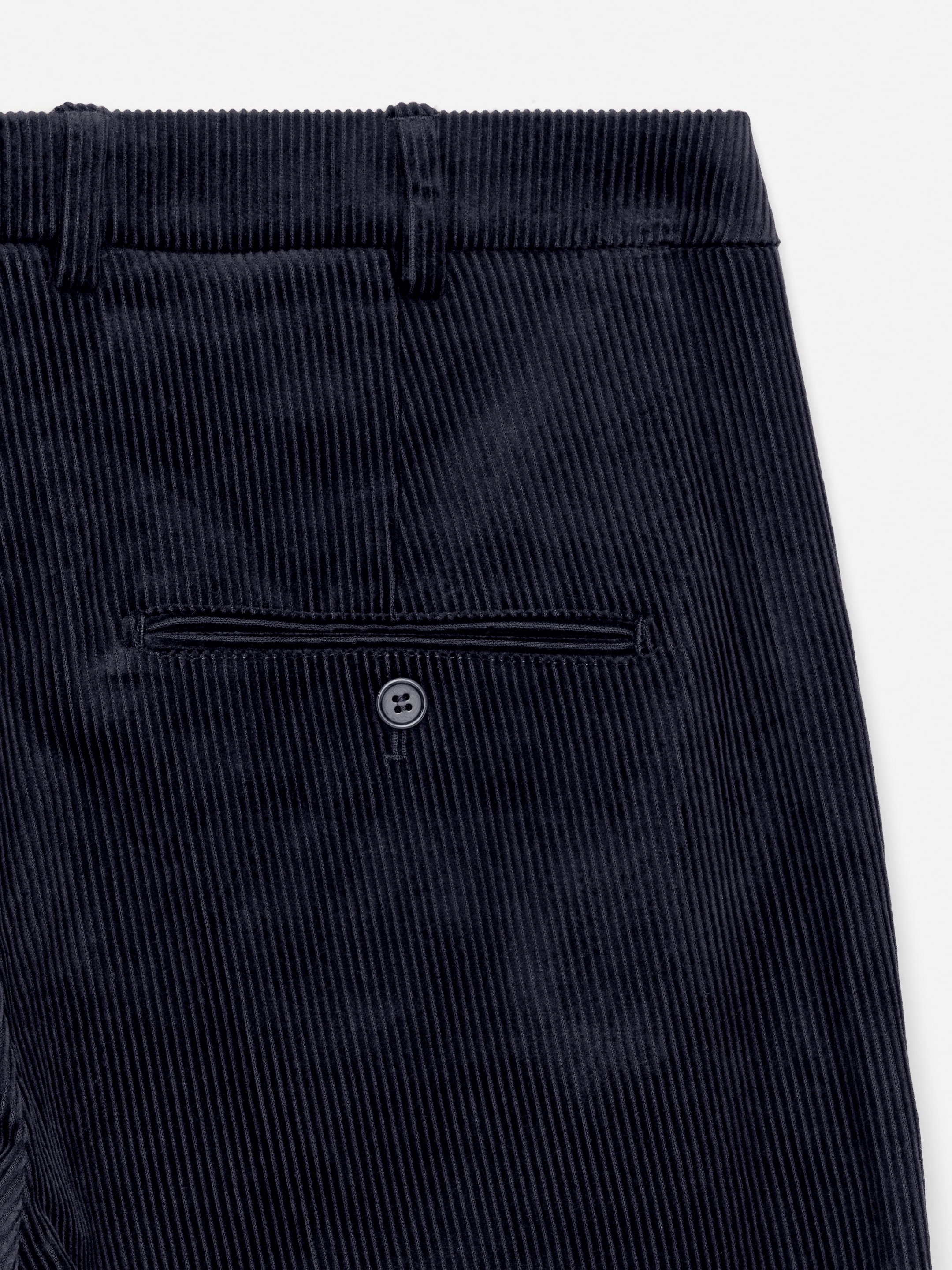 Ingrandisci l'immagine: Pantaloni di velluto a coste in una tonalità blu scuro sono presentati dal retro, con una cintura dotata di passanti per cintura e una tasca posteriore a filetto chiusa con un bottone.
