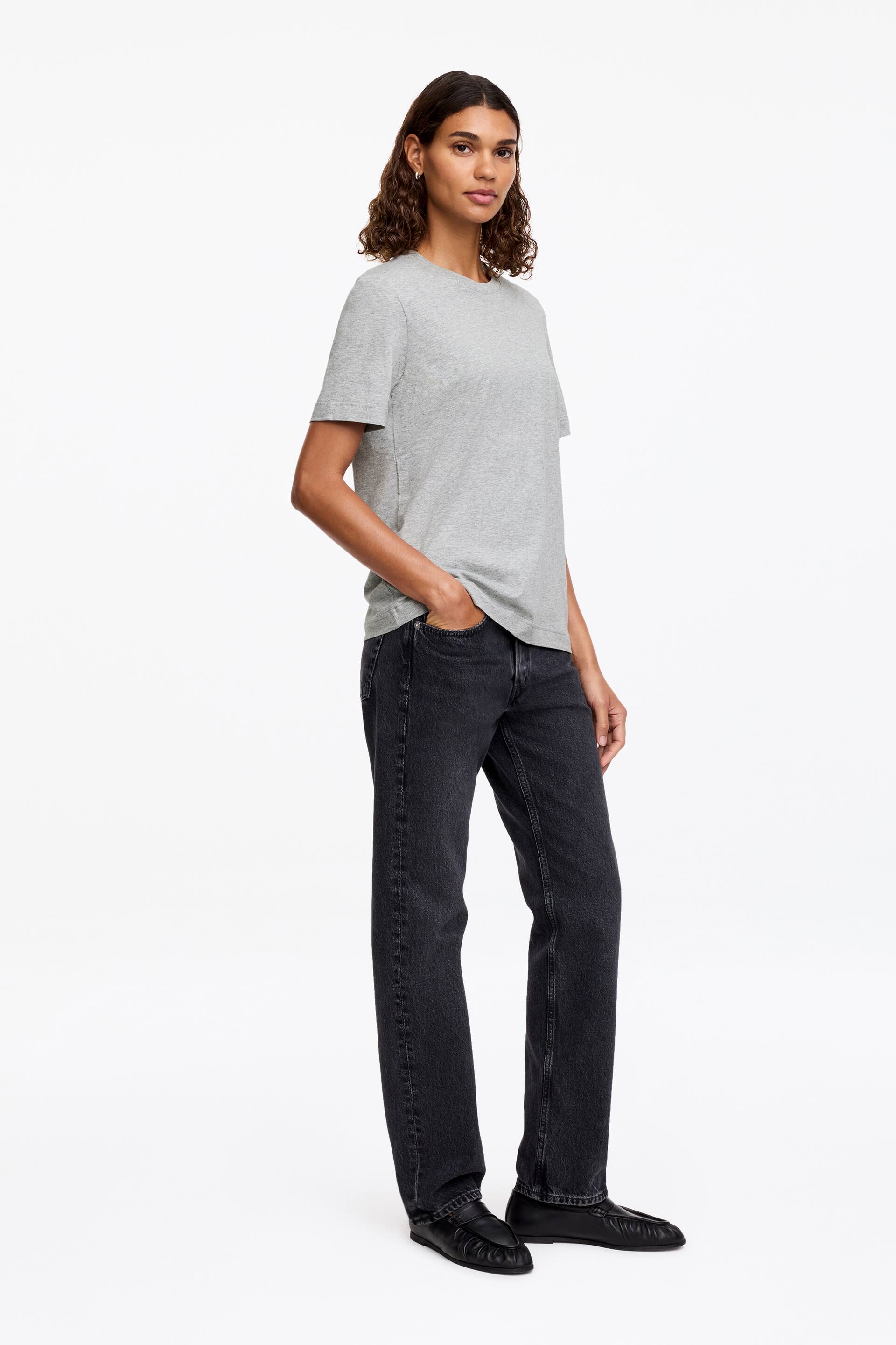 Grotere afbeelding bekijken: Een grijs T-shirt met een ronde hals en korte mouwen. De losse pasvorm valt soepel en is vooraan gedeeltelijk ingestopt in een donkere jeans.