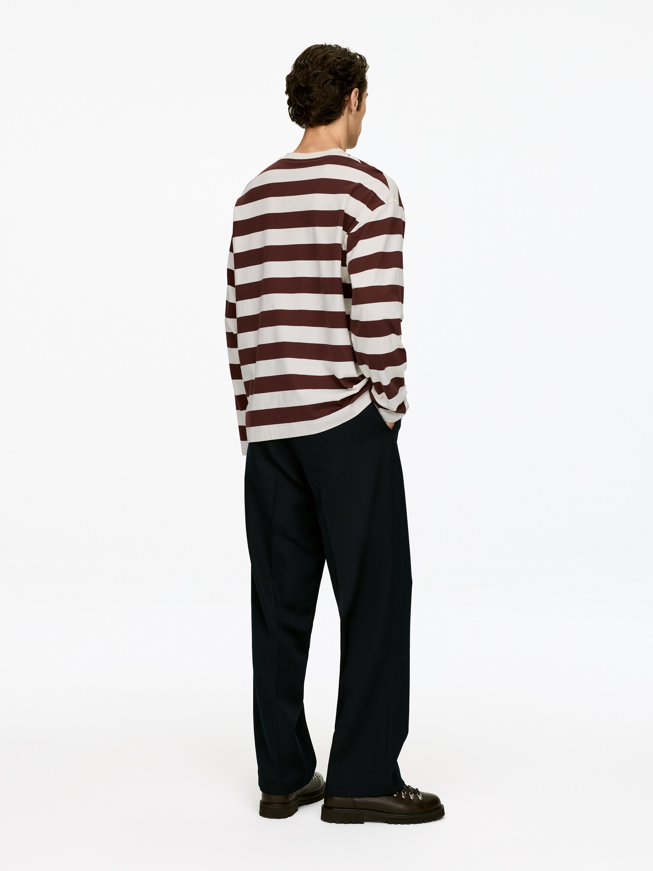 Agrandir l'image: Un haut à manches longues, avec des rayures horizontales alternant crème et marron, est assorti à un pantalon sombre, ample et des chaussures lacées épaisses de couleur foncée. La tenue est présentée de dos, avec la personne portant les vêtements légèrement tournée vers la droite.
