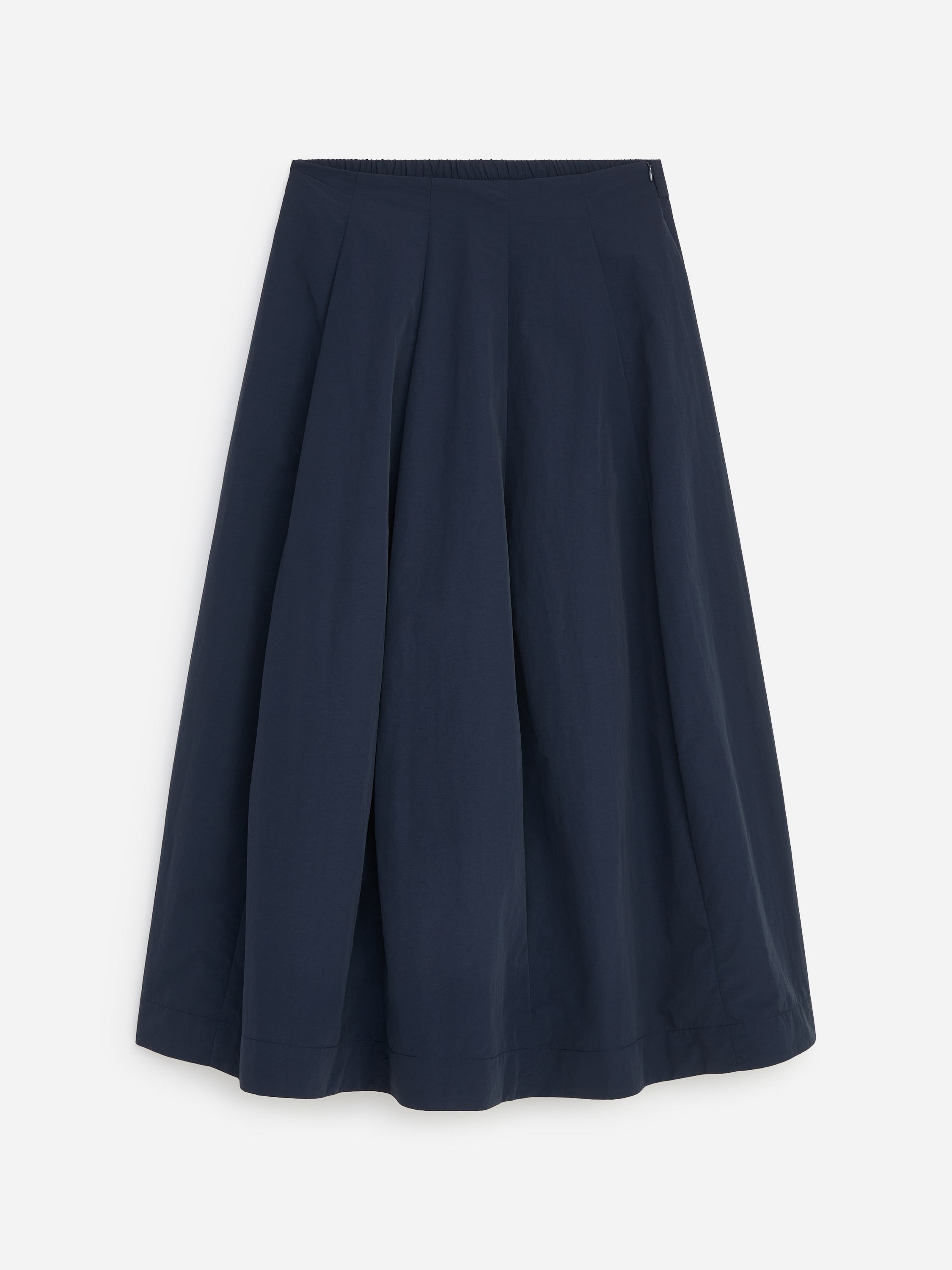 Malli yllÃ¤Ã¤n pitkÃ¤, tumman laivastonsininen nailonhame, jossa on runsaasti volyymia luova paneelirakenne. Hame on stailattu yhteensopivalla tumman laivastonsinisellÃ¤ half-zip-neuleella valkoisen T-paidan pÃ¤Ã¤llÃ¤, ja sen kanssa on yhdistetty mustat nahkasaappaat.