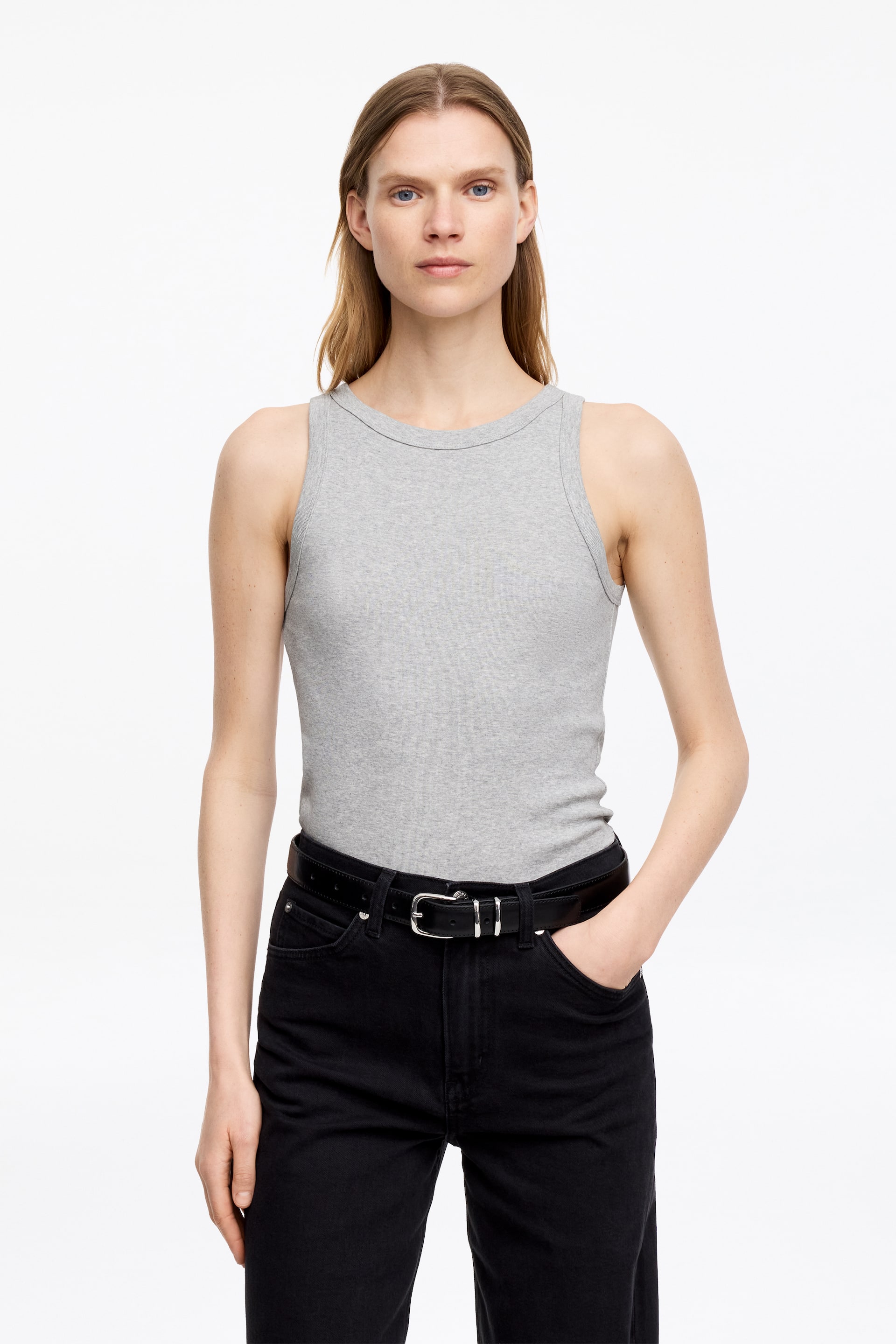 Größeres Bild anzeigen: Ein graues Tanktop aus gerippter Baumwoll-Jersey wird vom Model getragen. Breite Abschlüsse säumen den Halsausschnitt und die Armausschnitte. Das Model trägt es in schwarze Jeans gesteckt.
