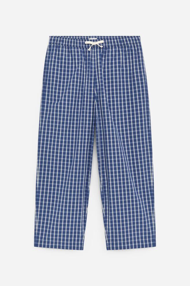 Die VORDERSEITE der blau-weiß karierten Hose zeigt einen elastischen Bund mit einem weißen Kordelzug, der zu einer Schleife gebunden ist. Gerade Hosenbeine erstrecken sich nach unten und enden in einfachen Säumen. - 1