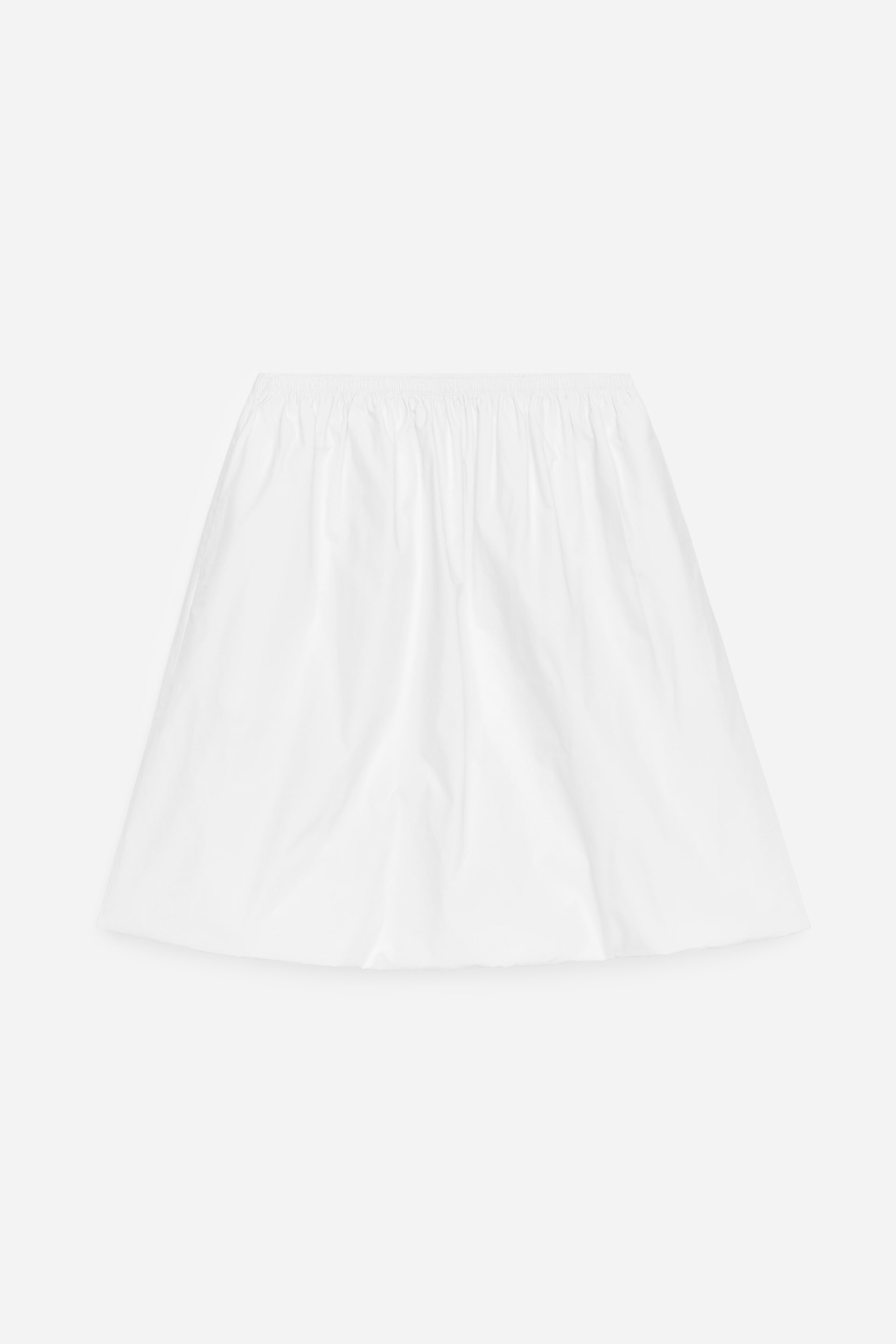Visa större bild: En vit kjol visas FRAM, med en rynkad, elastisk midja och en utsvängd, A-linjeformad silhuett. Det släta vita tyget visar mjuka draperingar.