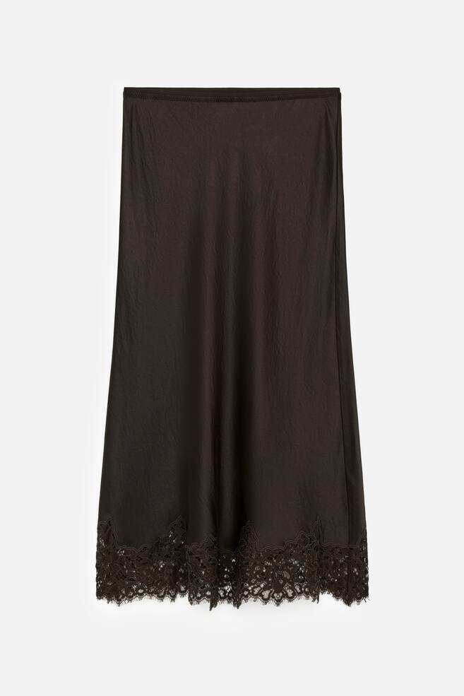 The front of a black bias-cut satin skirt is being presented. It is designed with an elastic waistband and is showcasing intricate lace detailing along its fluted hem. - 1