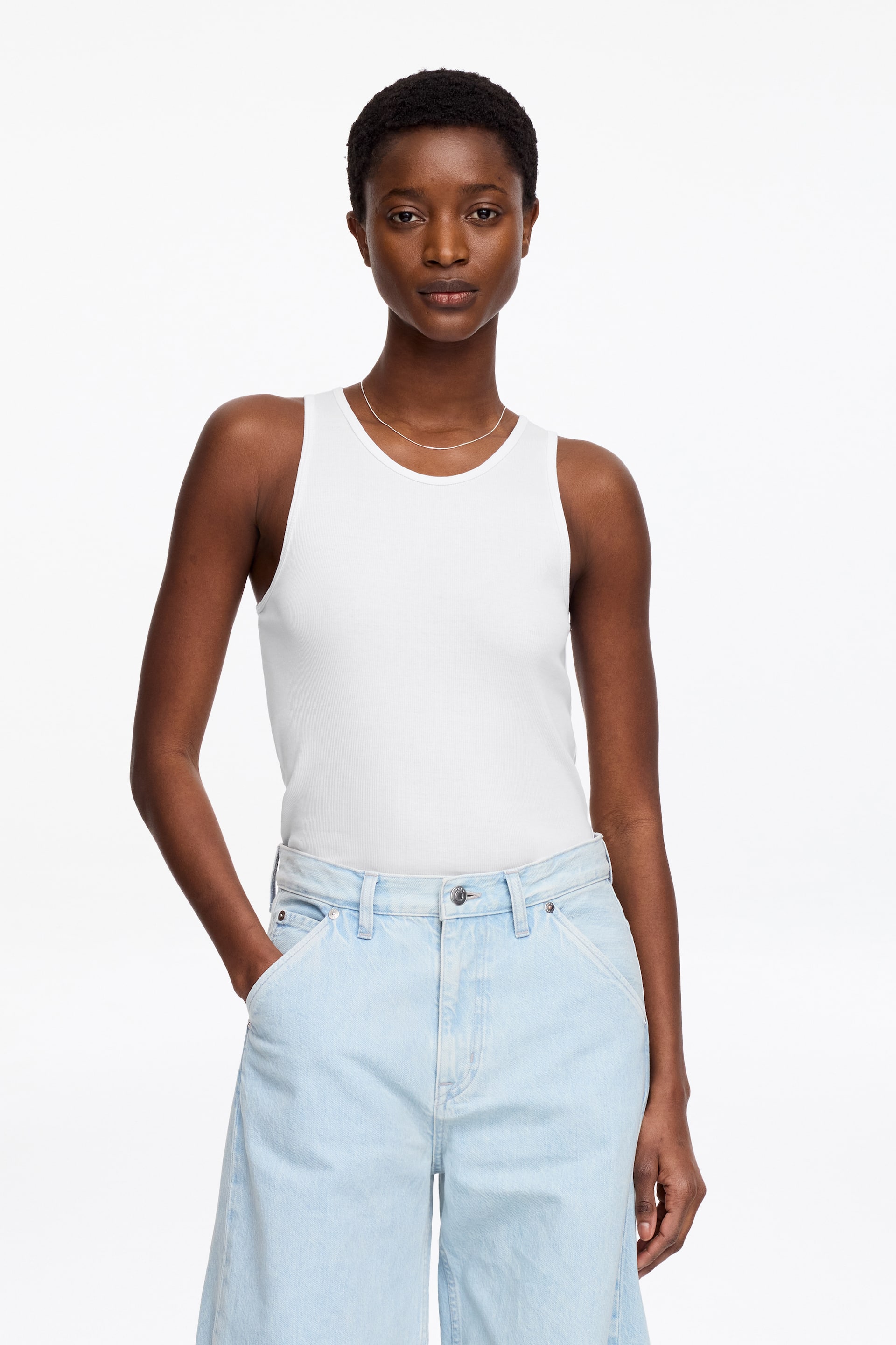 View larger image: A white ribbed vest is being presented facing forward, featuring a round neckline and sleeveless design. It fits closely to the torso, showcasing its structured fit.