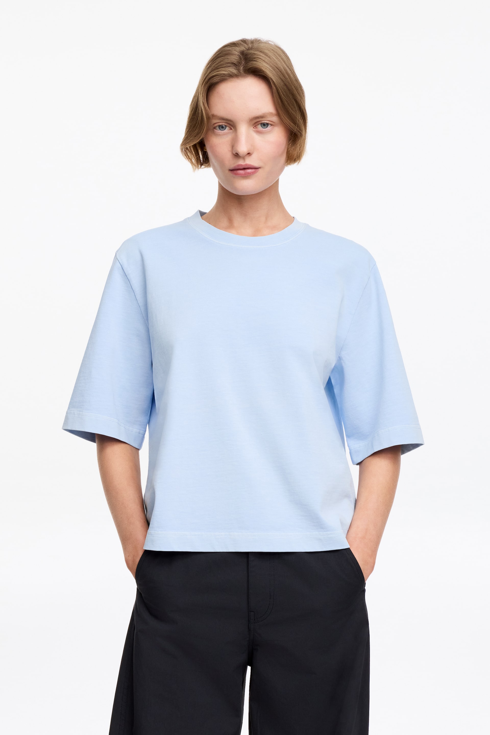 Agrandir l'image: Un t-shirt bleu clair à col rond est présenté, face avant. Il présente une coupe ample et carrée avec des manches courtes et larges ainsi qu'un ourlet droit, et des coutures blanches détaillent l'encolure.