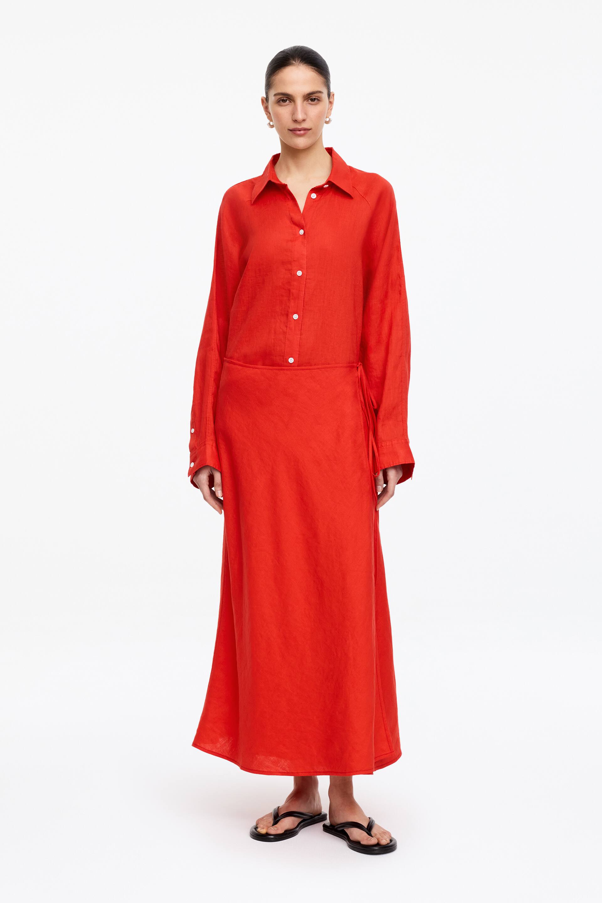View larger image: A red textured long-sleeved shirt dress is showcased, featuring a pointed collar, a full button-front placket with white buttons, and buttoned cuffs. The dress is cinched at the waist with a tie detail and flows into a maxi-length skirt.