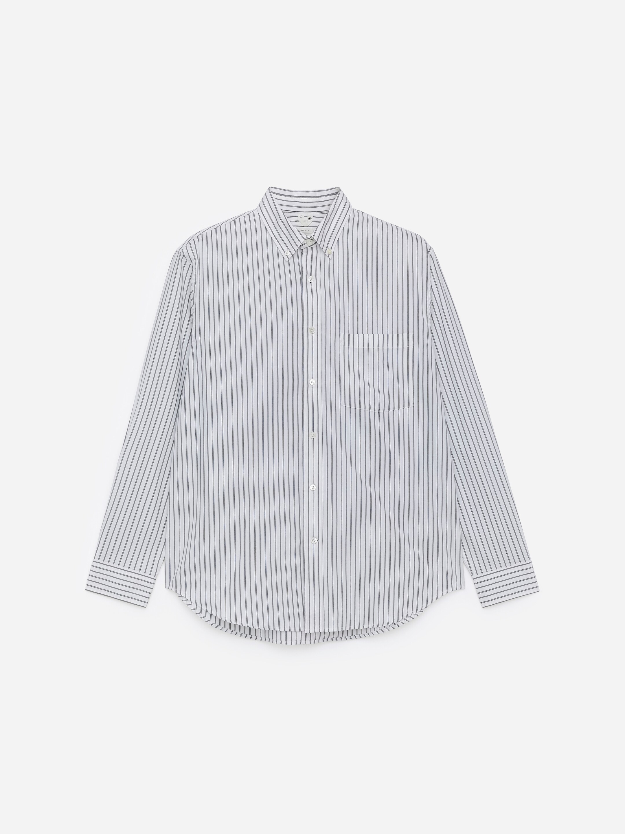 Visualizza immagine più grande: Una camicia bianca a maniche lunghe con sottili strisce verticali scure viene presentata dal davanti, caratterizzata da un colletto con bottoni, una chiusura frontale con bottoni chiari e una tasca singola sul petto a sinistra. Presenta anche polsini con bottoni e un orlo arrotondato.