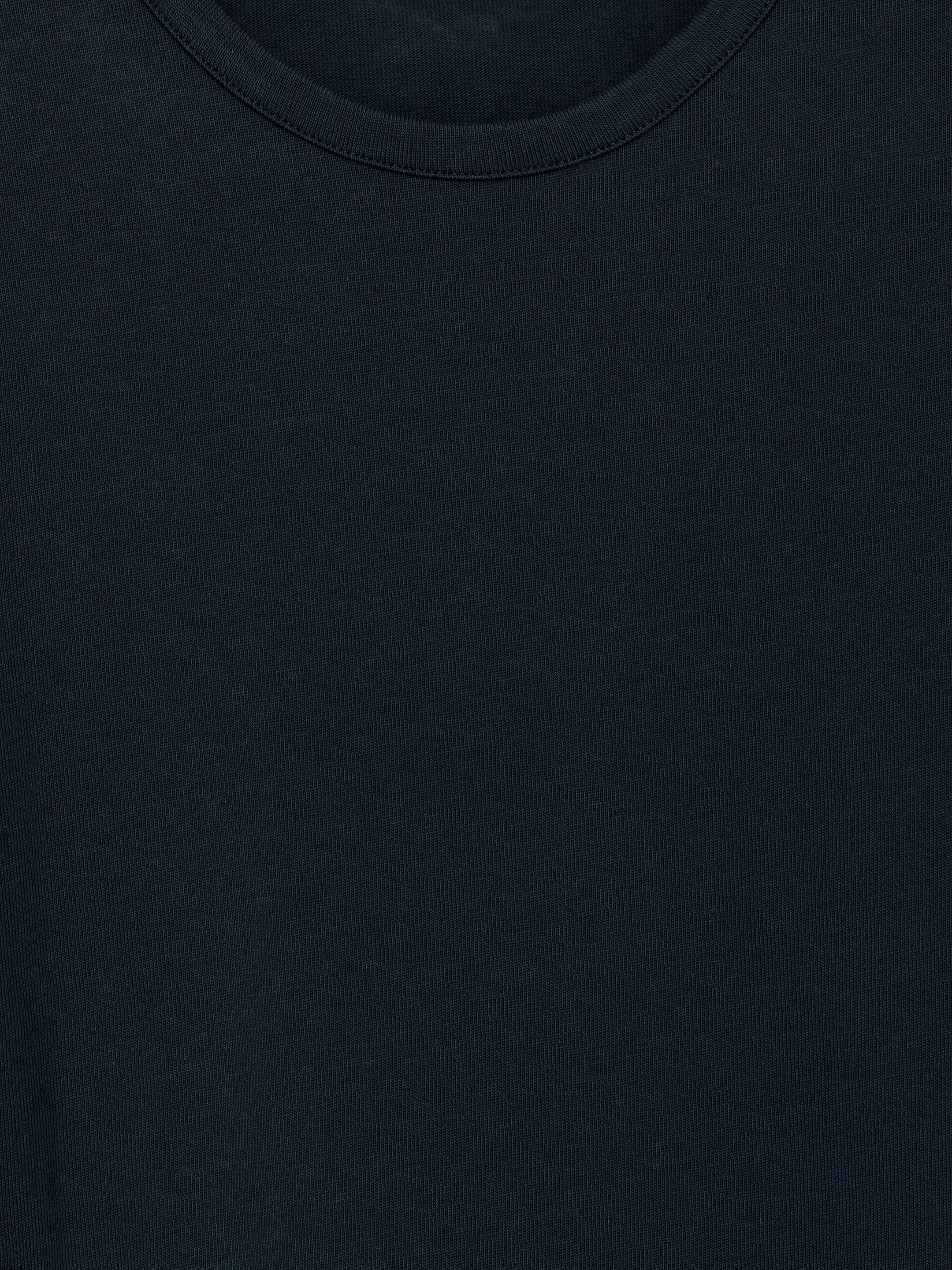 Visa större bild: En mörktonad T-shirt med rund hals presenteras platt på framsidan, med en ribbad halsringning och en fint stickad textur.