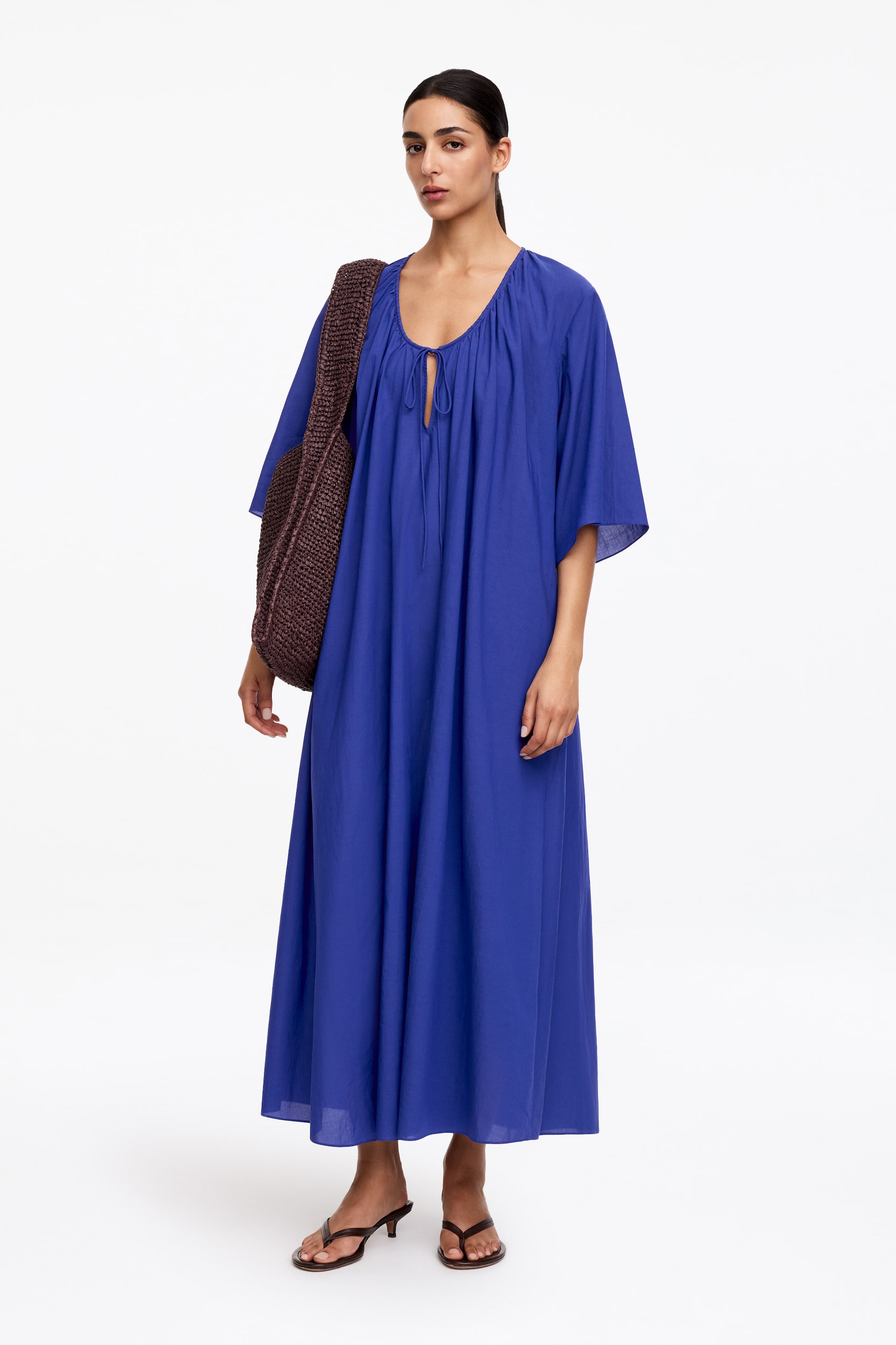 View larger image: The blue maxi dress features a gathered V-neckline with ties and wide, elbow-length sleeves. Its loose, flowing silhouette extends to the ankles.