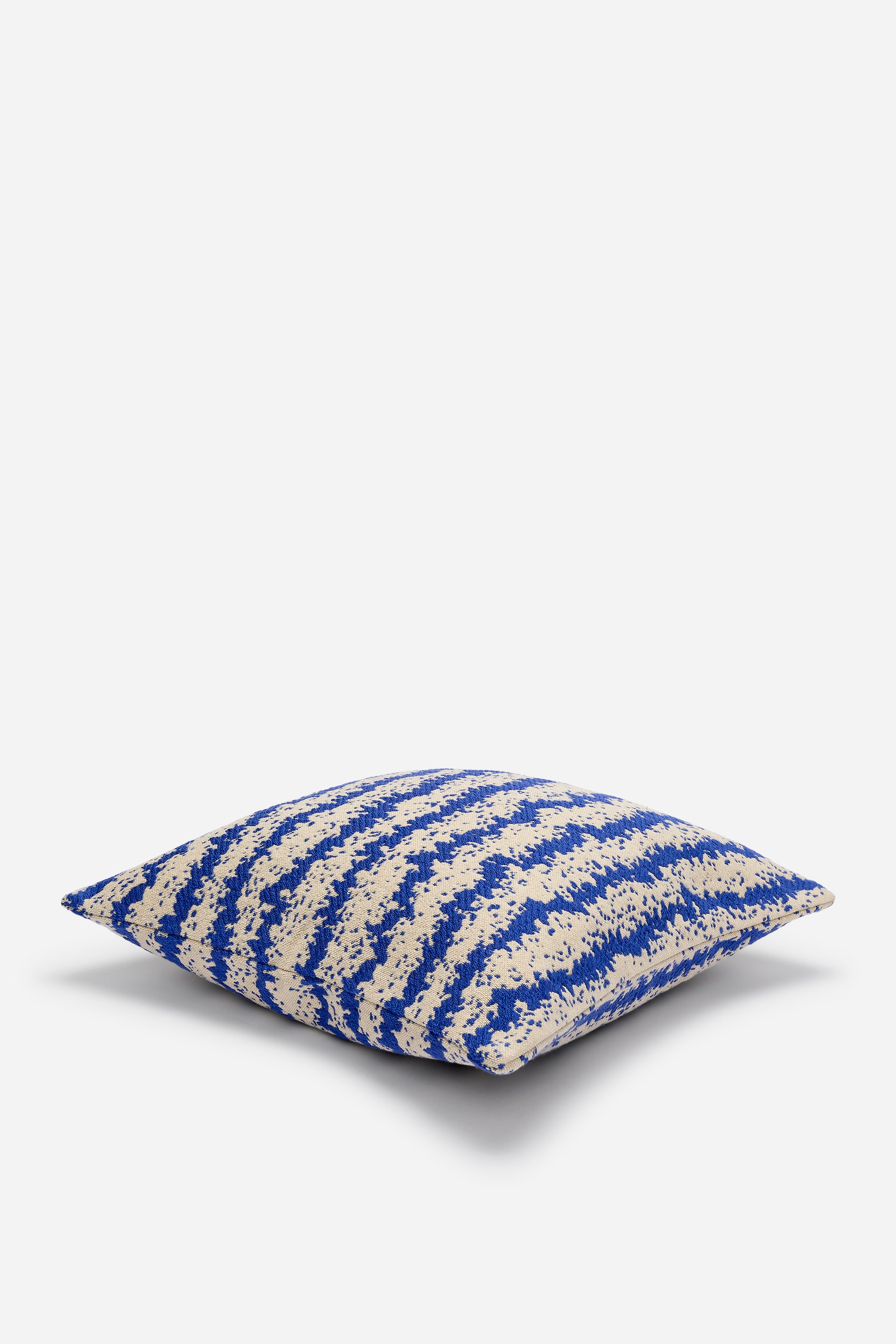 Преглед на по-голямо изображение: Квадратна възглавница представя модел от хоризонтални, неправилни сини ивици върху бежов фон. Сините ивици се отличават с видимо текстурирана, на петна повърхност.