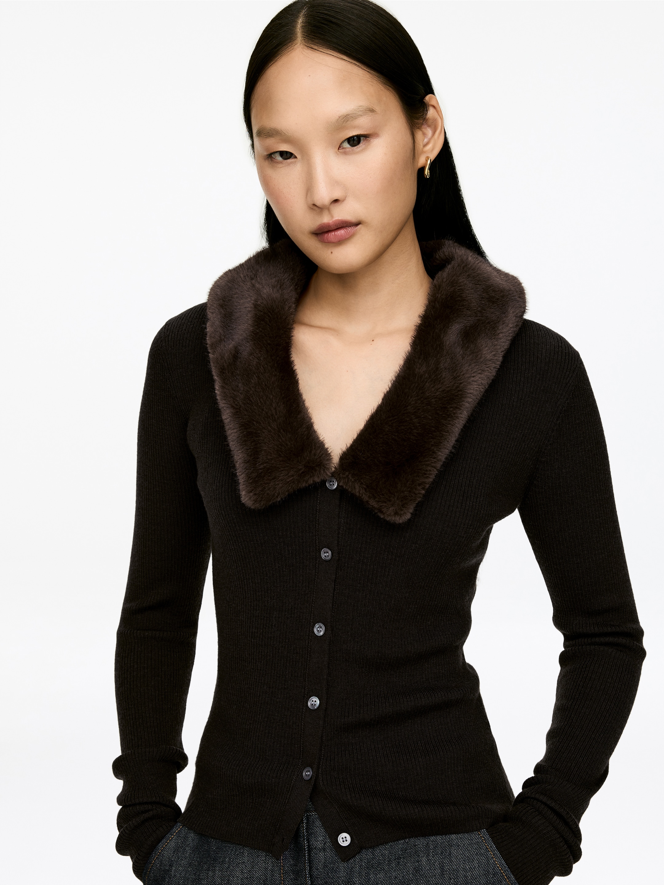 Größeres Bild ansehen: Eine dunkelbraune gerippte Strickjacke präsentiert sich vorne, mit einem plüschigen dunkelbraunen Kunstfellkragen. Sie ist mit einem Knopfverschluss vorne und langen Ärmeln versehen, die hellfarbige Knöpfe zur Schau stellen.