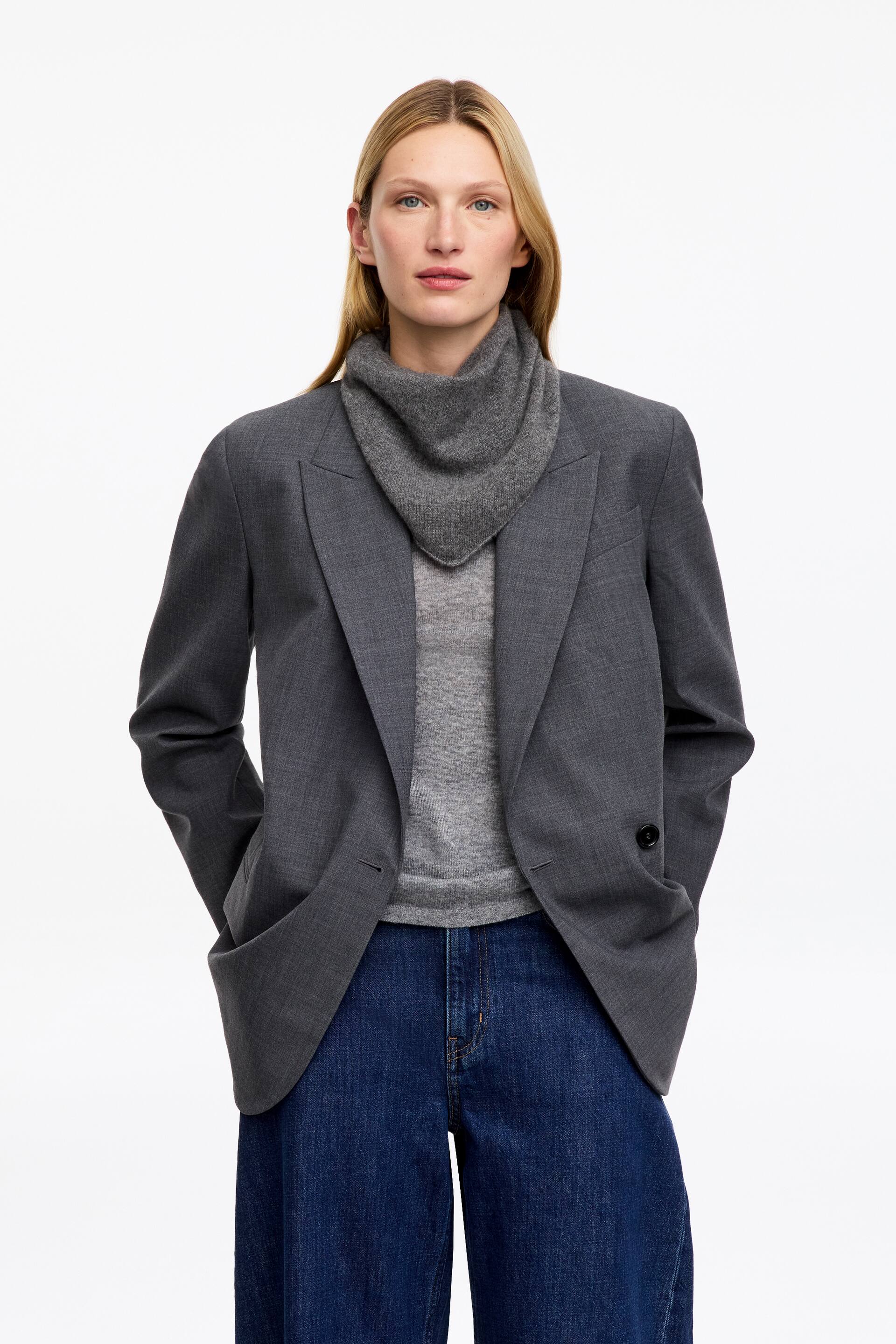 Ver imagen más grande: La modelo lleva una pequeña bufanda gris, doblada en forma triangular y enrollada alrededor del cuello. Va superpuesta sobre un top gris y debajo de un blazer gris.