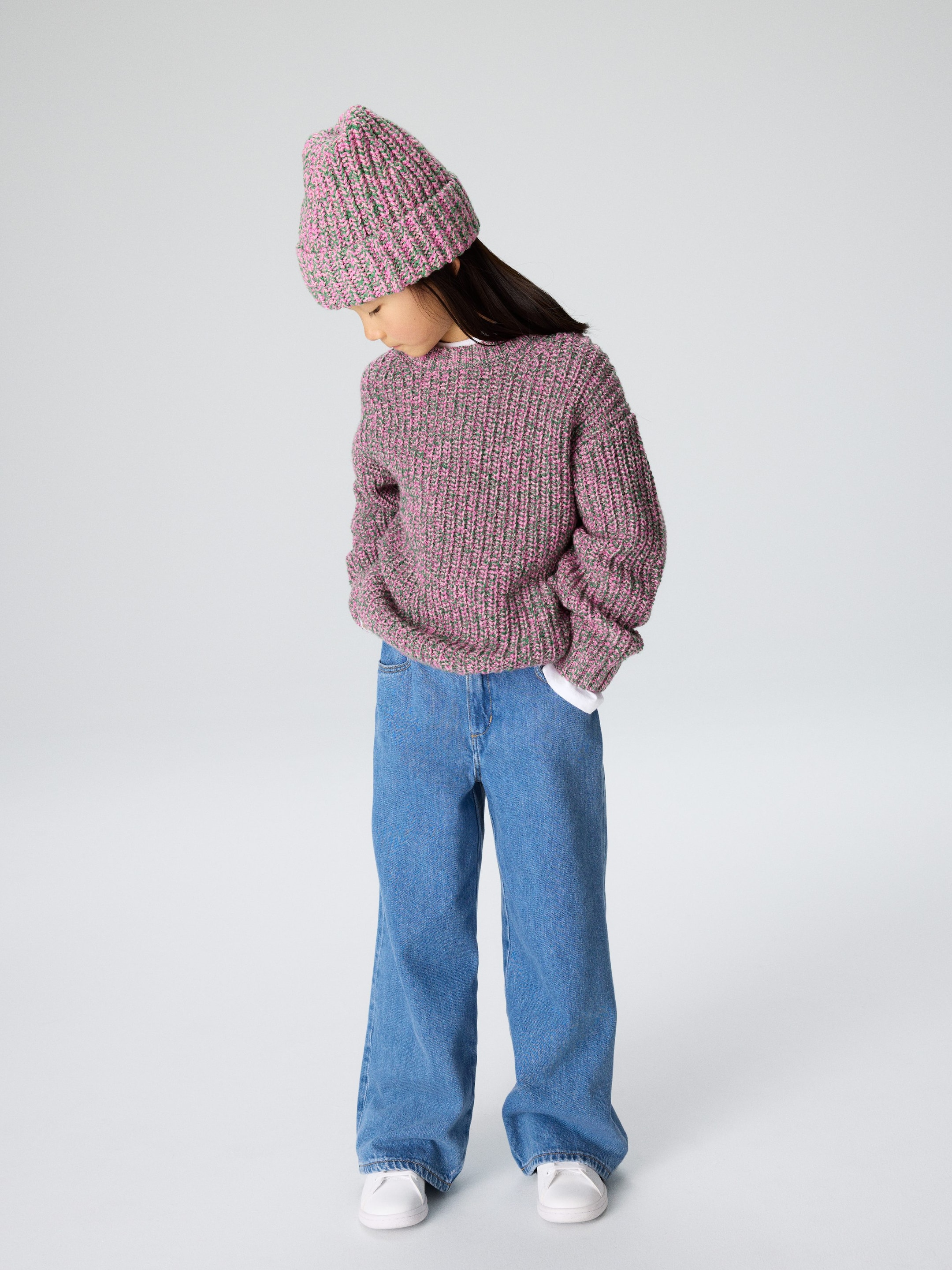 Ver imagen más grande: Se lleva un gorro de punto acanalado jaspeado en rosa y verde, inclinado ligeramente hacia la izquierda. Un jersey a juego de cuello redondo y talla grande, con una camisa blanca debajo, se combina con unos vaqueros de pierna ancha y lavado claro, y unas zapatillas blancas.