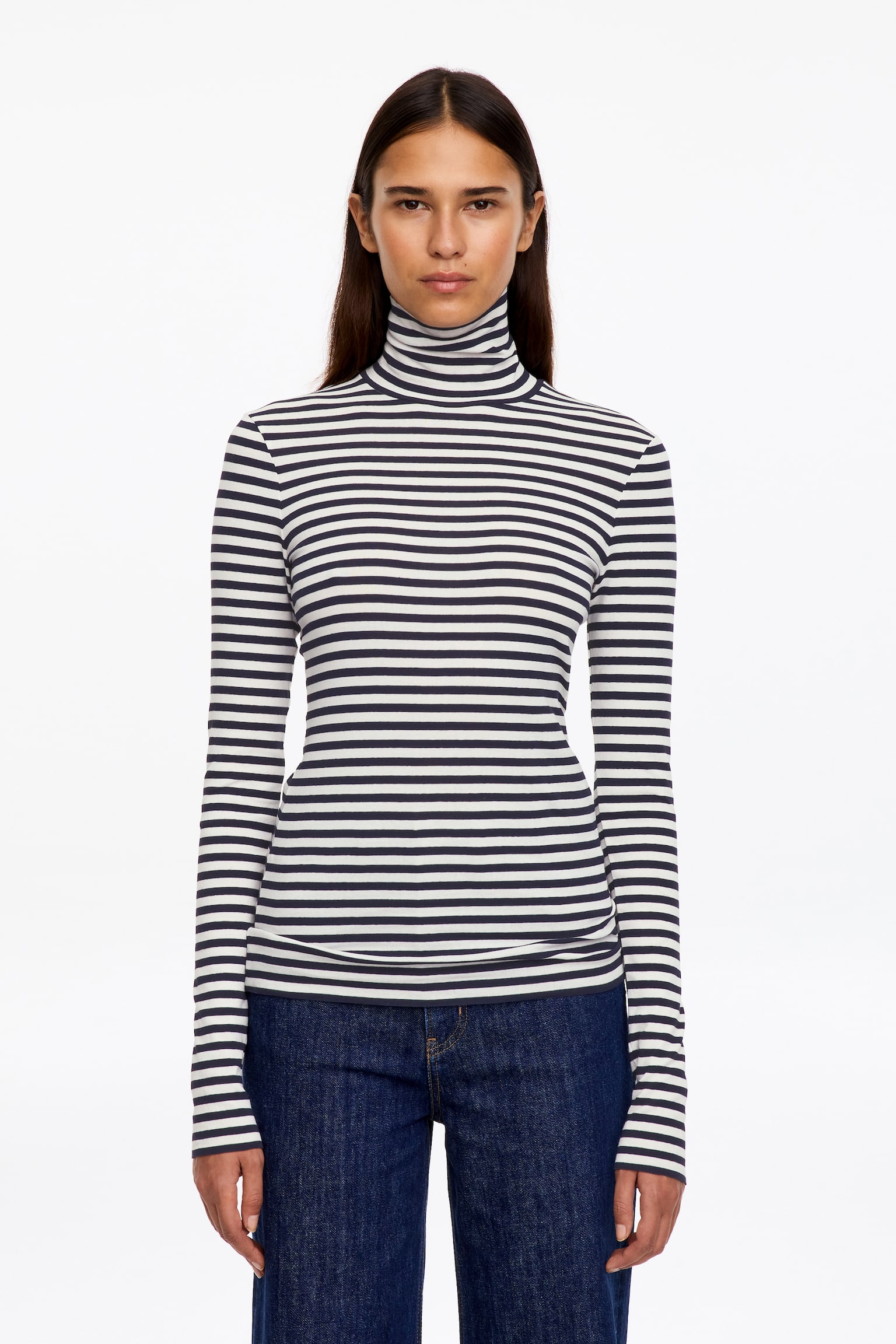 Een jersey top met lange mouwen en col, uitgevoerd met donkere en witte horizontale strepen, wordt gedragen door het model. De aansluitende top is gecombineerd met donkerblauwe denim jeans. - 1