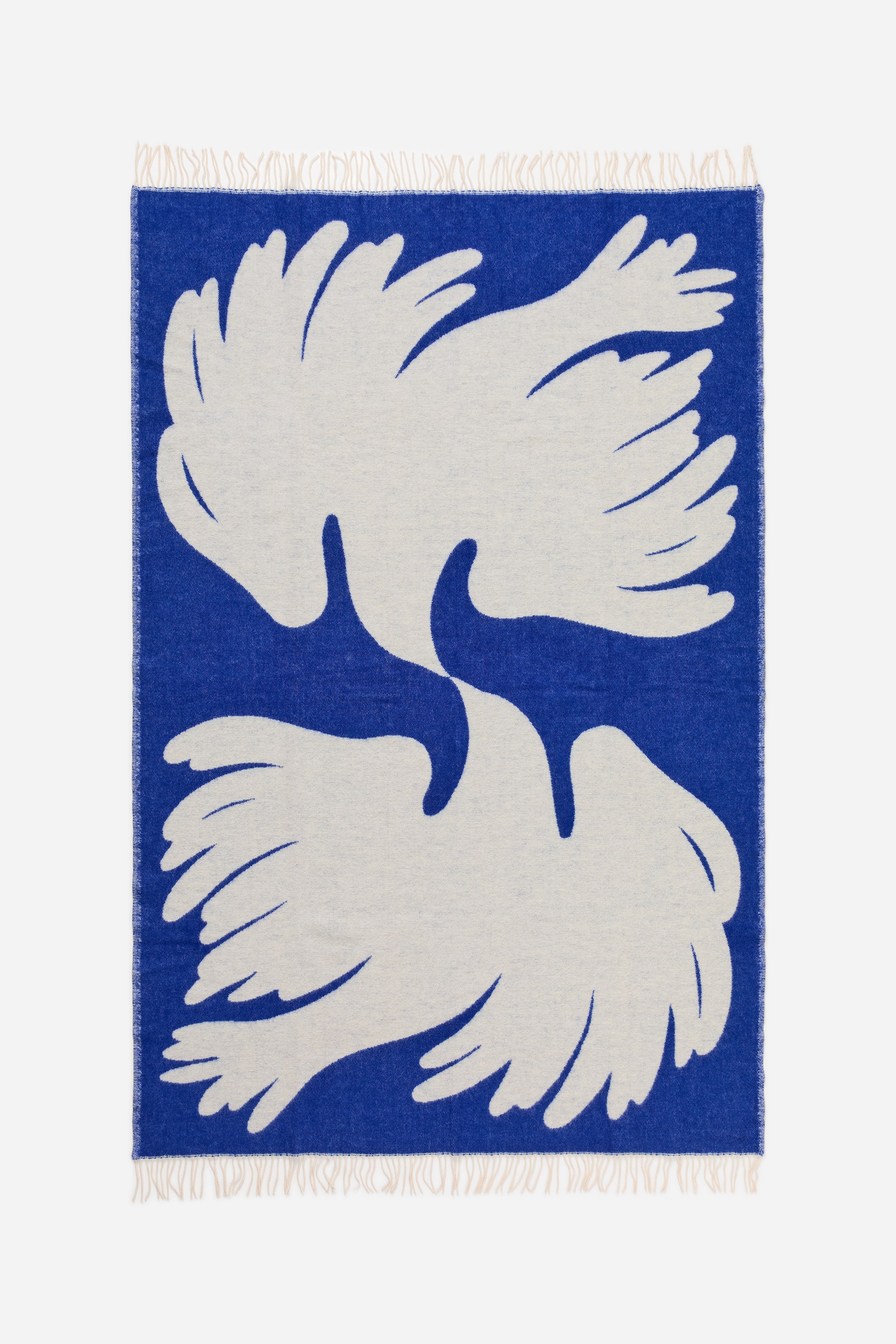 Visa större bild: En rektangulär textilpläd med ett djupt blått fält pryds av två stora, benvita abstrakta fågelformer och kort, ljus frans längs dess övre och nedre kanter.