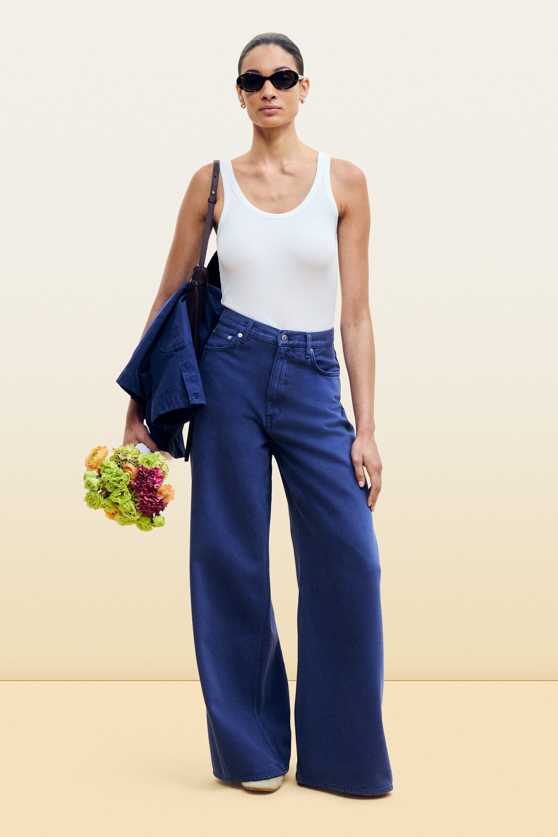 Visa större bild: En vit tanktop med en rundad hals och tunna axelband bärs instoppad i mörkblåa jeans med vida ben.