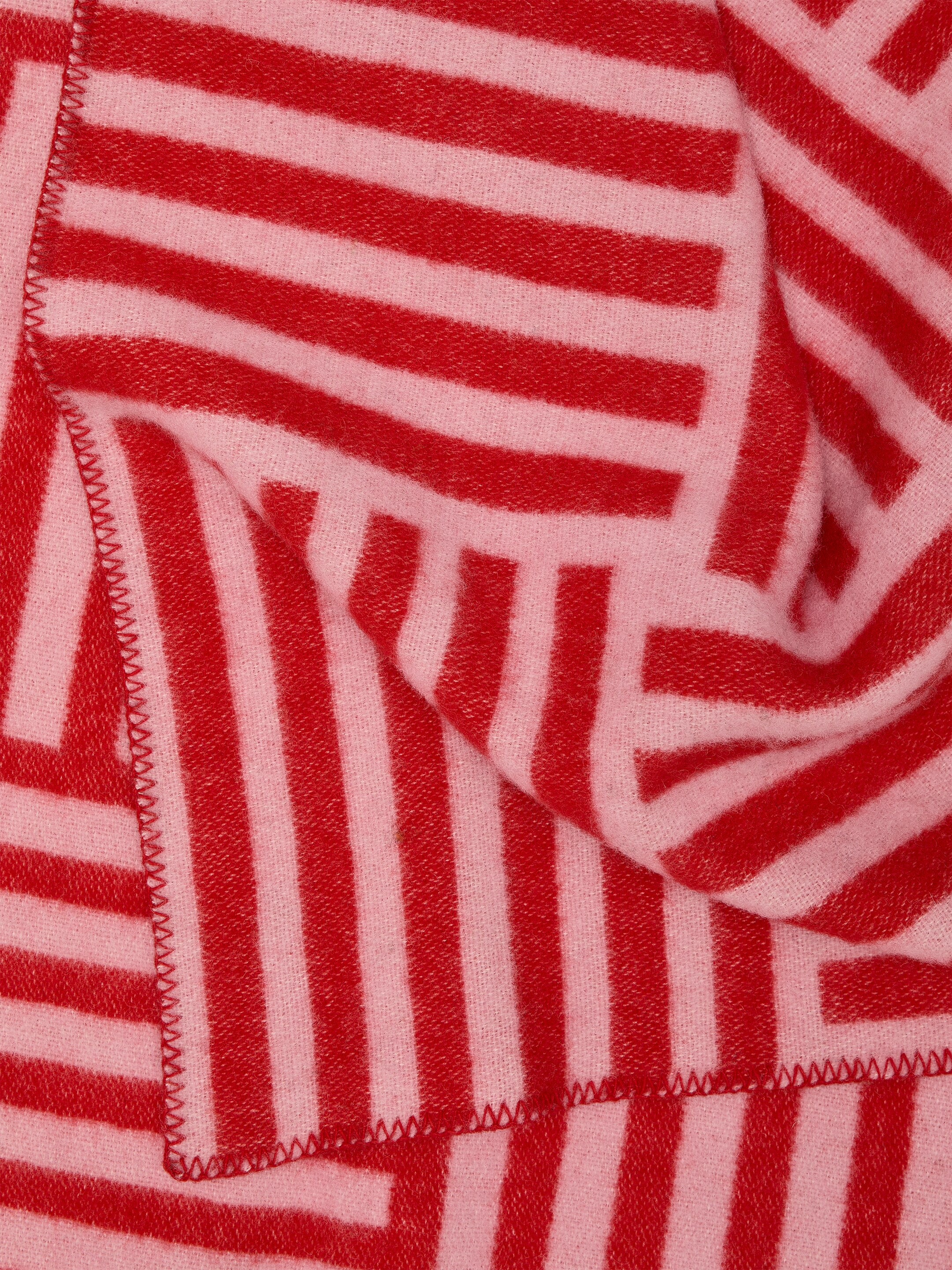 Visa större bild: En textil visar ett mönster av skärningspunkterna mellan röda och ljusrosa ränder, som bildar en geometrisk design. Det mjuka, vävda materialet har zig-zag sydda kanter och det hänger för att visa sin struktur och varierande randorienteringar.