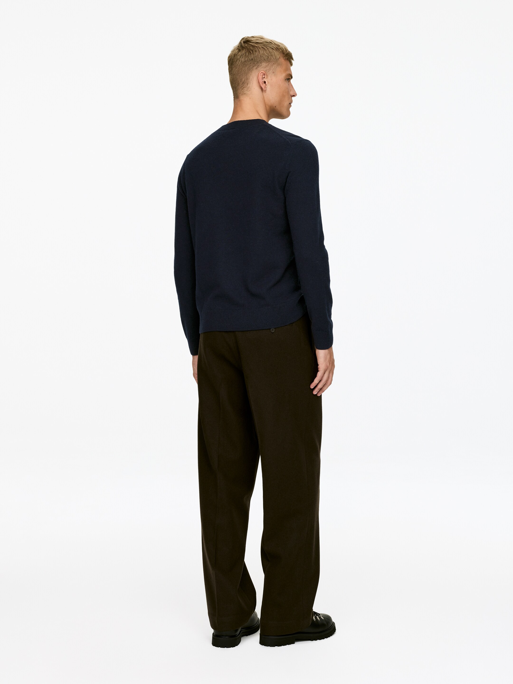 Agrandir l'image: Un pull bleu foncé est présenté de dos, légèrement tourné vers la droite. Il présente un col rond classique, des manches longues et une texture finement tricotée avec un ourlet droit.