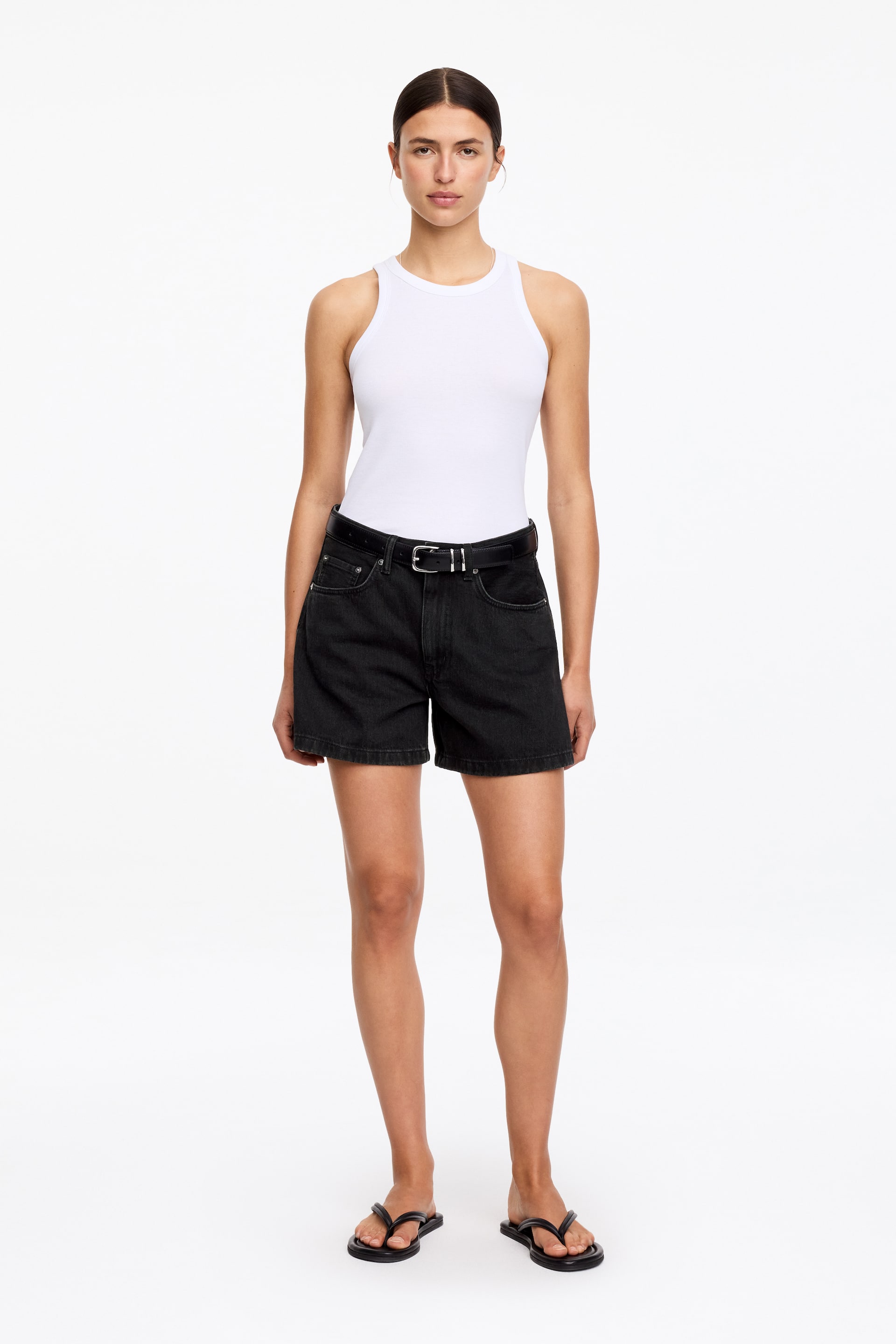 Agrandir l'image: Les shorts en denim noir sont présentés de face, avec une coupe taille haute et jambe droite qui s'arrête au-dessus du genou. Une ceinture noire est passée dans les passants de ceinture.