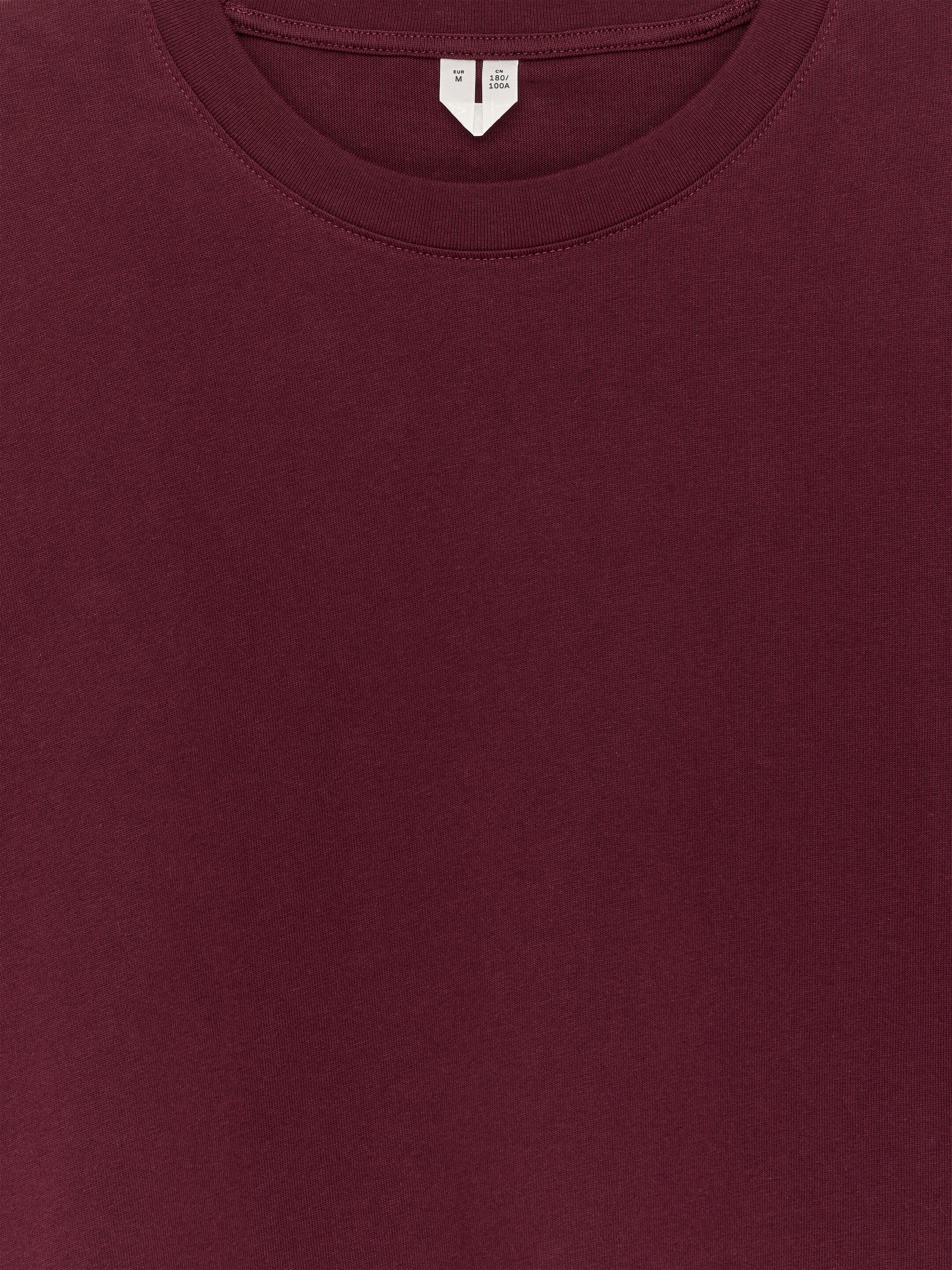 Agrandir l'image: Un T-shirt en coton à manches longues de couleur bordeaux foncé est présenté de face, avec un col rond doté d'une bande de col côtelée et une étiquette blanche visible à l'arrière du cou.