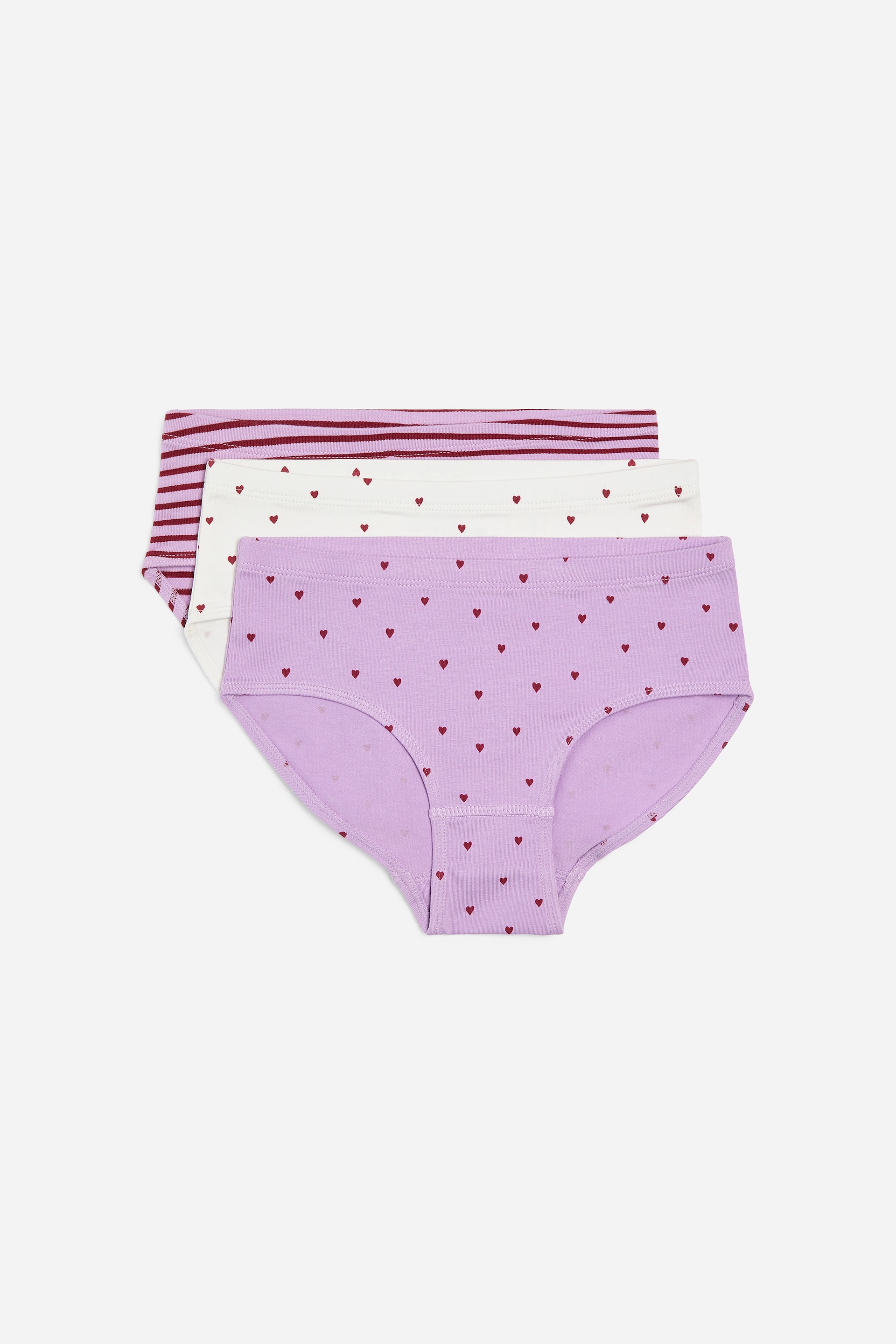 Agrandir l'image: Trois paires de slips sont empilées et présentées sous un angle légèrement incliné. La paire du haut est violette avec un motif de cœurs rouges, celle du milieu est blanche avec un motif de cœurs rouges, et la paire du bas est d'un violet clair avec des rayures horizontales bordeaux.