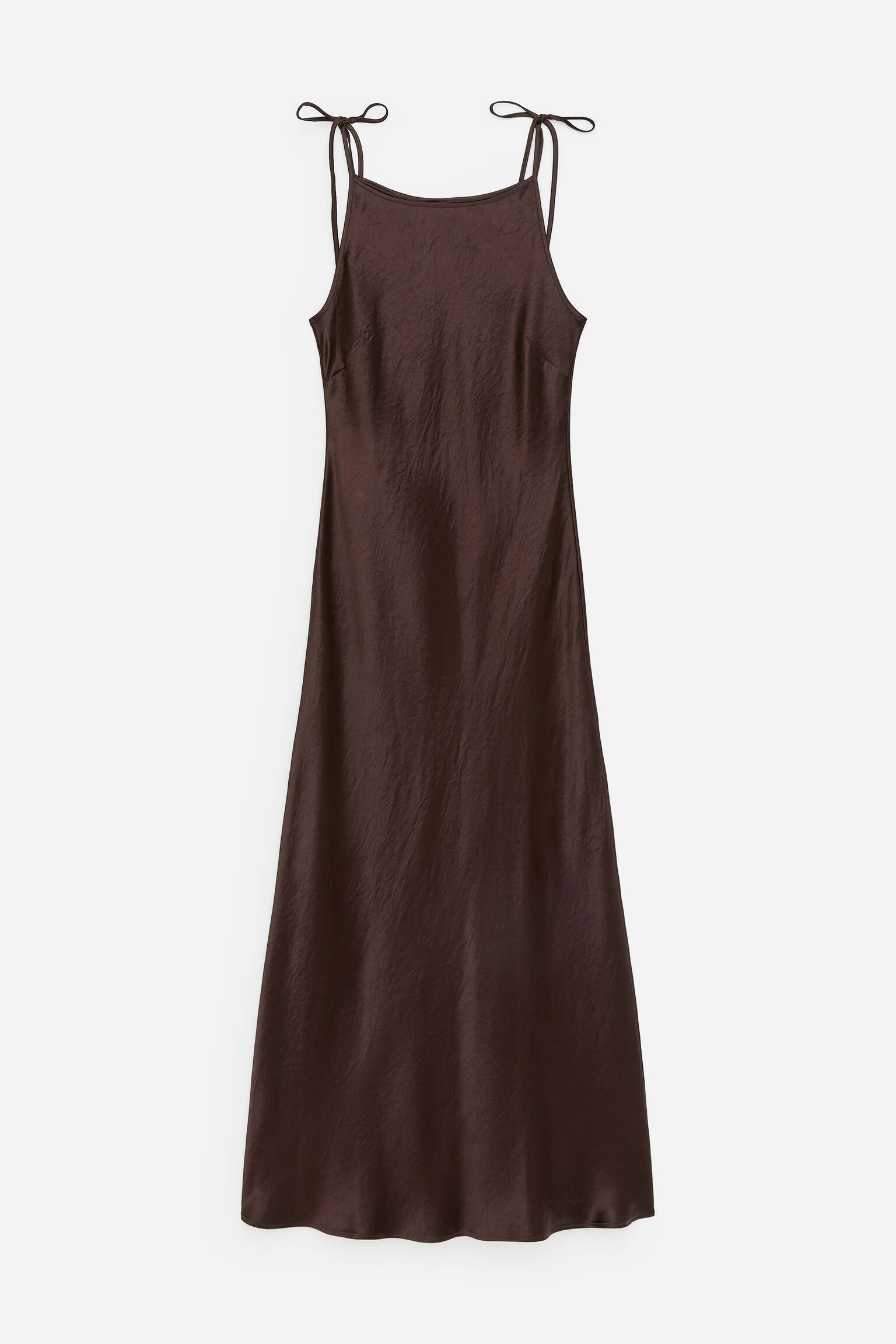 Ein dunkelbraunes Midi-Slip-Kleid mit geknitterter Textur, präsentiert einen quadratischen Ausschnitt und dünne Spaghettiträger, die zu Schleifen an den Schultern gebunden sind, und fließt in eine A-Linien-Silhouette.