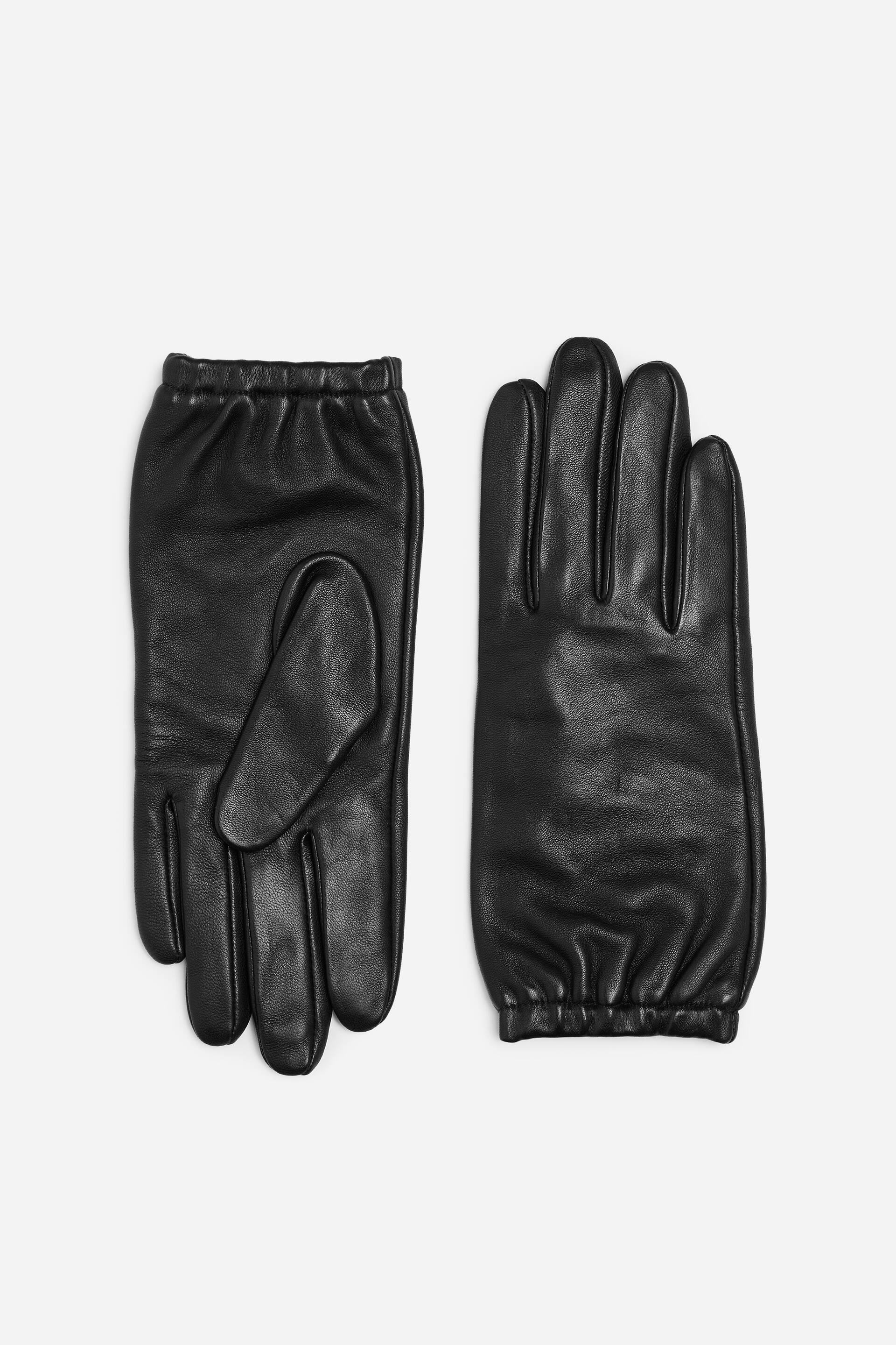 View larger image: Black leather gloves are lying flat, with one glove showing the back of the hand and the other showing the palm. Both gloves feature individual finger sections and gathered wrist cuffs.