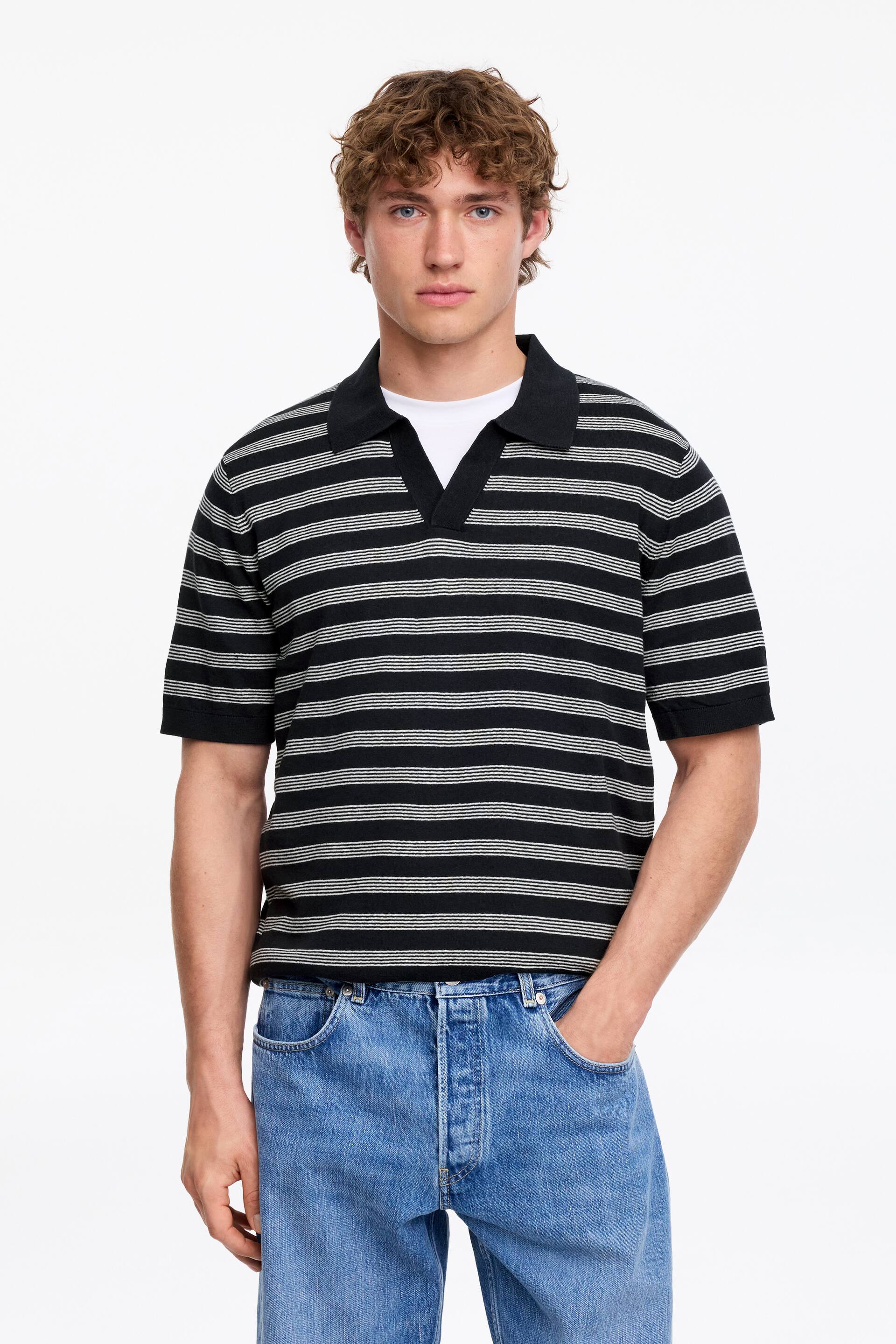 Grösseres Bild ansehen: Ein schwarz-weiß fein gestreiftes Strick-Poloshirt mit einem Spread-Kragen und einer V-Ausschnitt-Knopfleiste wird über einem weißen Rundhals-T-Shirt getragen.