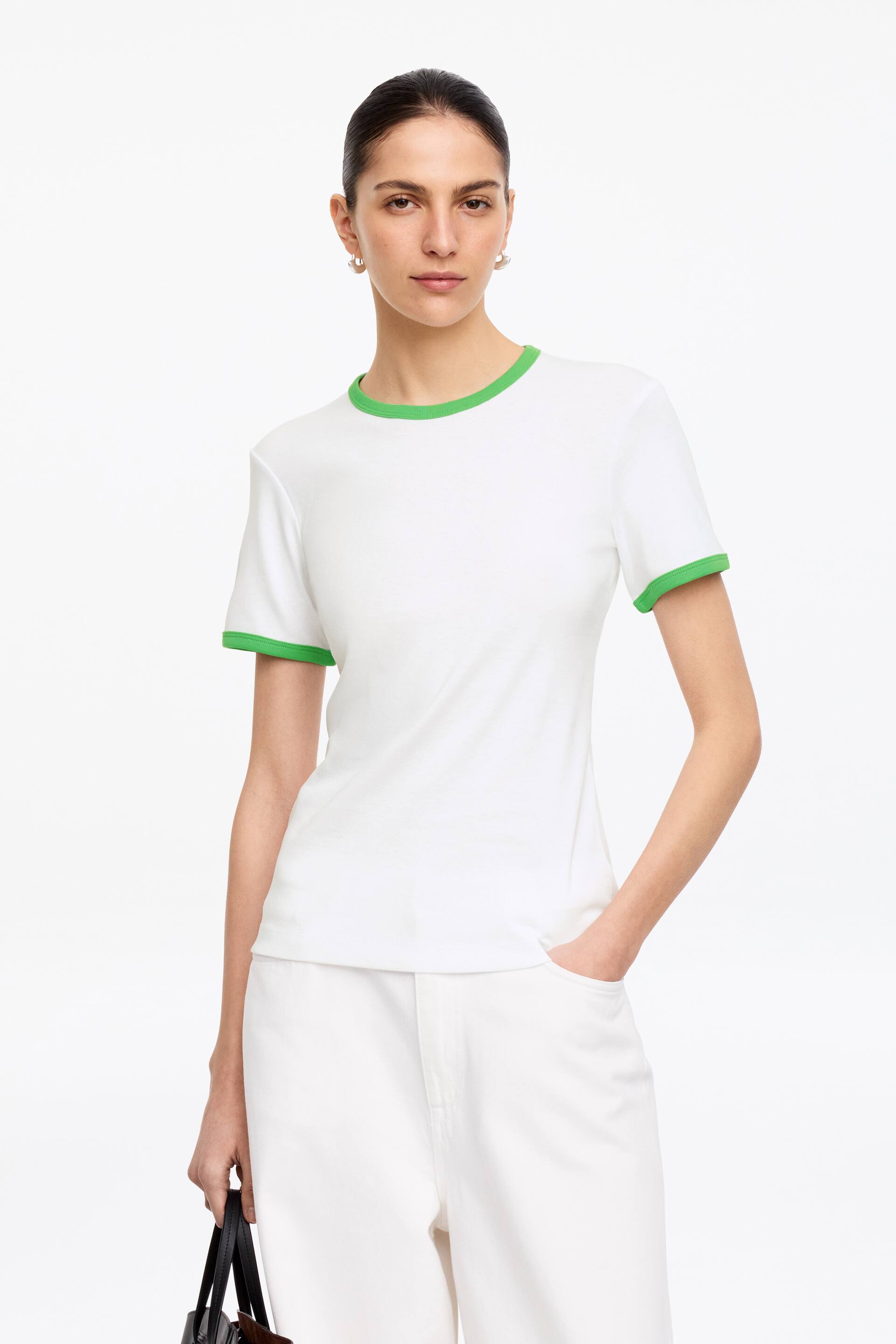 Grotere afbeelding bekijken: Een wit t-shirt met korte mouwen, met een groene bies langs de ronde hals en mouwboorden, sluit nauw aan op het lichaam vanuit een vooraanzicht.