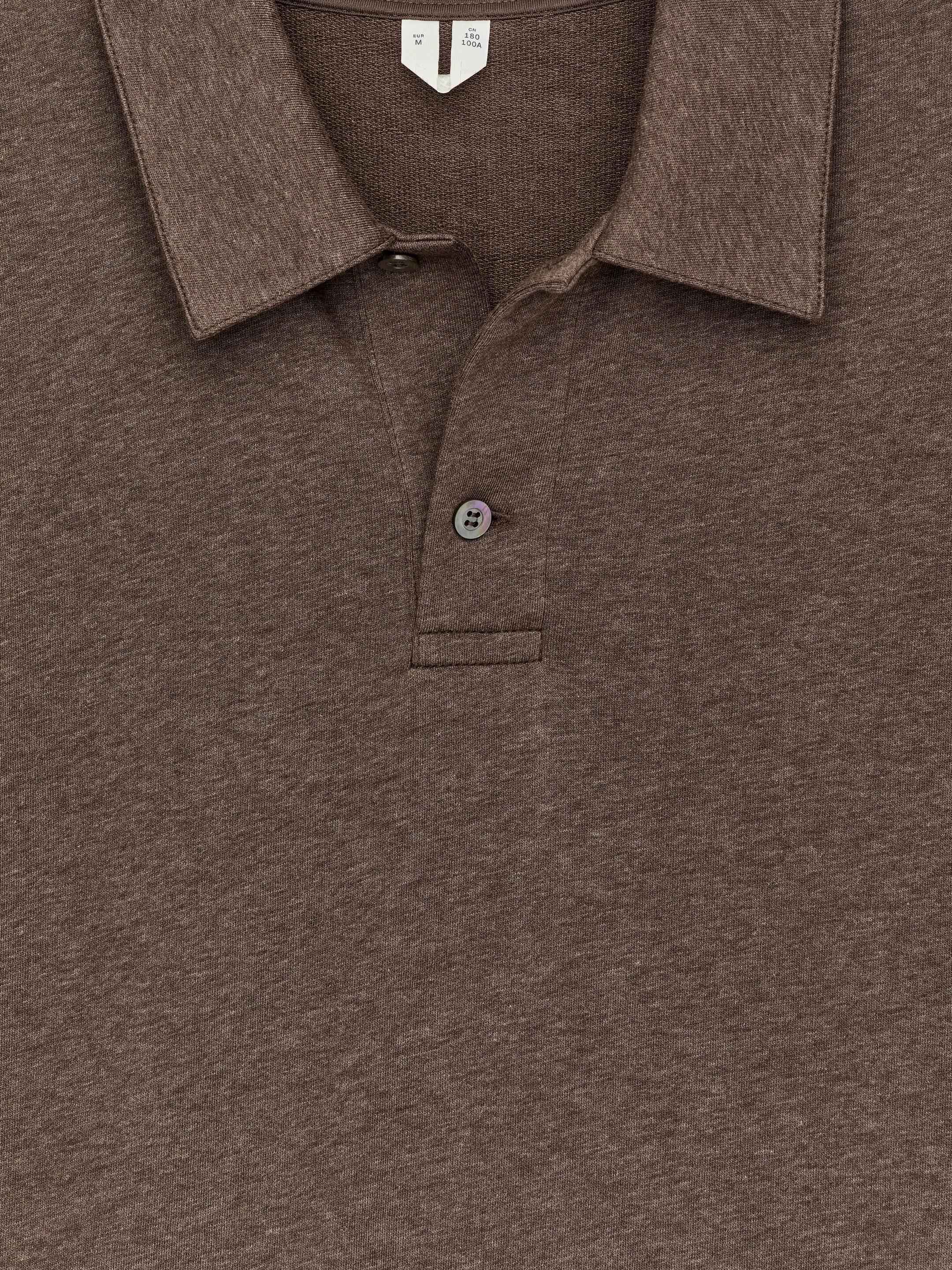 Größeres Bild ansehen: Ein brauner Feinstrick-Pullover mit Polo-Kragen wird von vorne gezeigt, mit einem normalen Kragen und einer halben Knopfleiste mit zwei dunklen, schillernden Knöpfen. Der Stoff hat eine melierte, feinstrukturierte Textur.