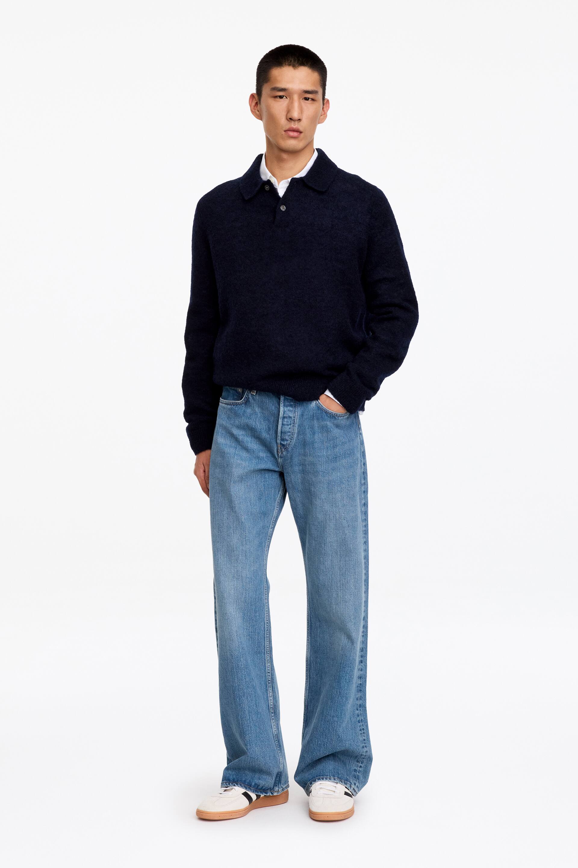 Visualizza l'immagine ingrandita: Jeans in denim lavato azzurro chiaro con vita media, vestibilità regolare e gamba boot-cut, indossati dalla modella che è in piedi con una mano appoggiata nella tasca anteriore. I jeans sono abbinati a un maglione polo a maniche lunghe blu navy scuro e sneaker bianche.
