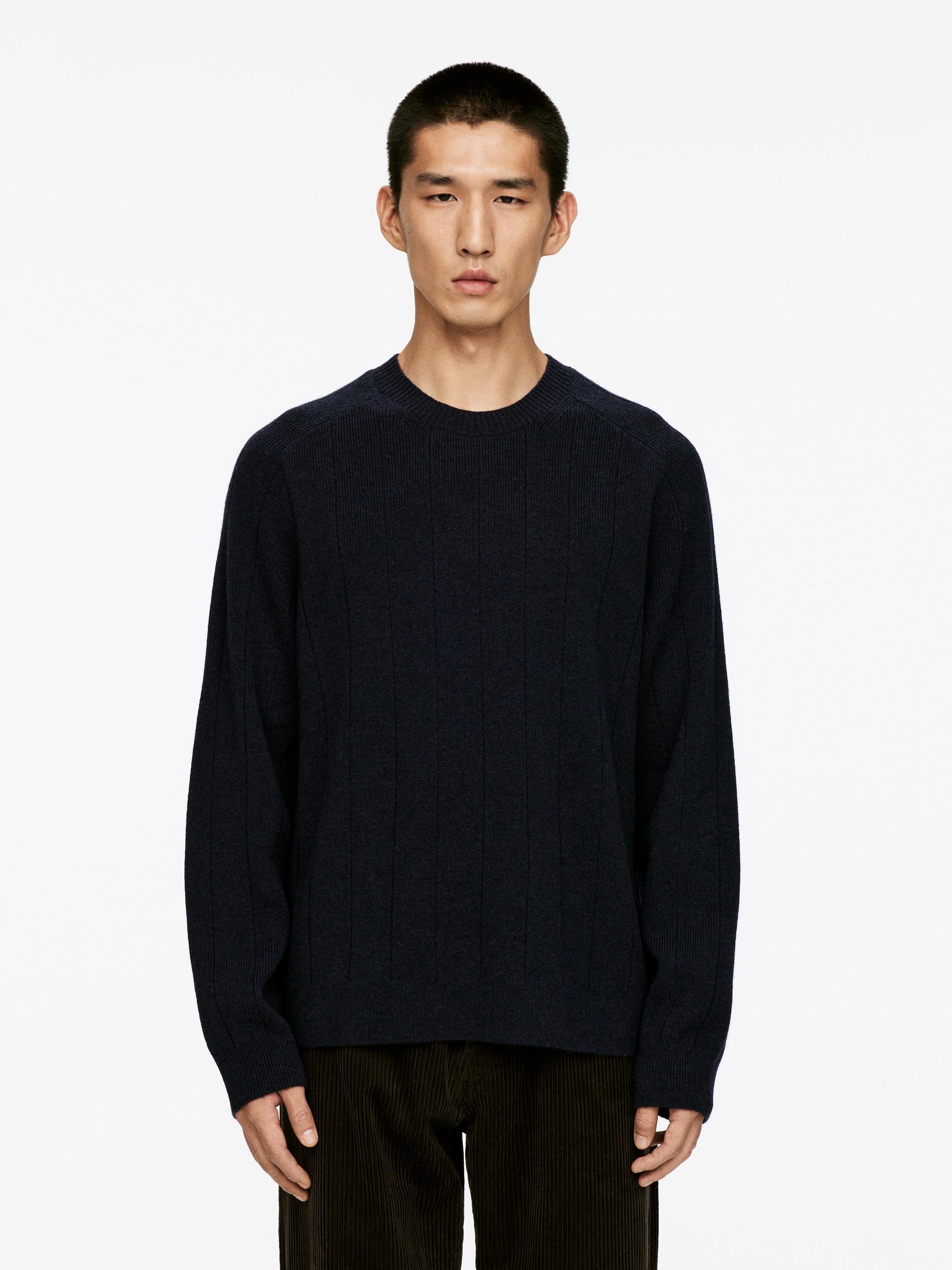 View larger image: A dark blue crew neck sweater is being presented, facing forward. It is featuring prominent vertical ribbed detailing throughout its body and sleeves, with ribbed cuffs and a ribbed hem. The sweater is being shown over dark brown corduroy pants.