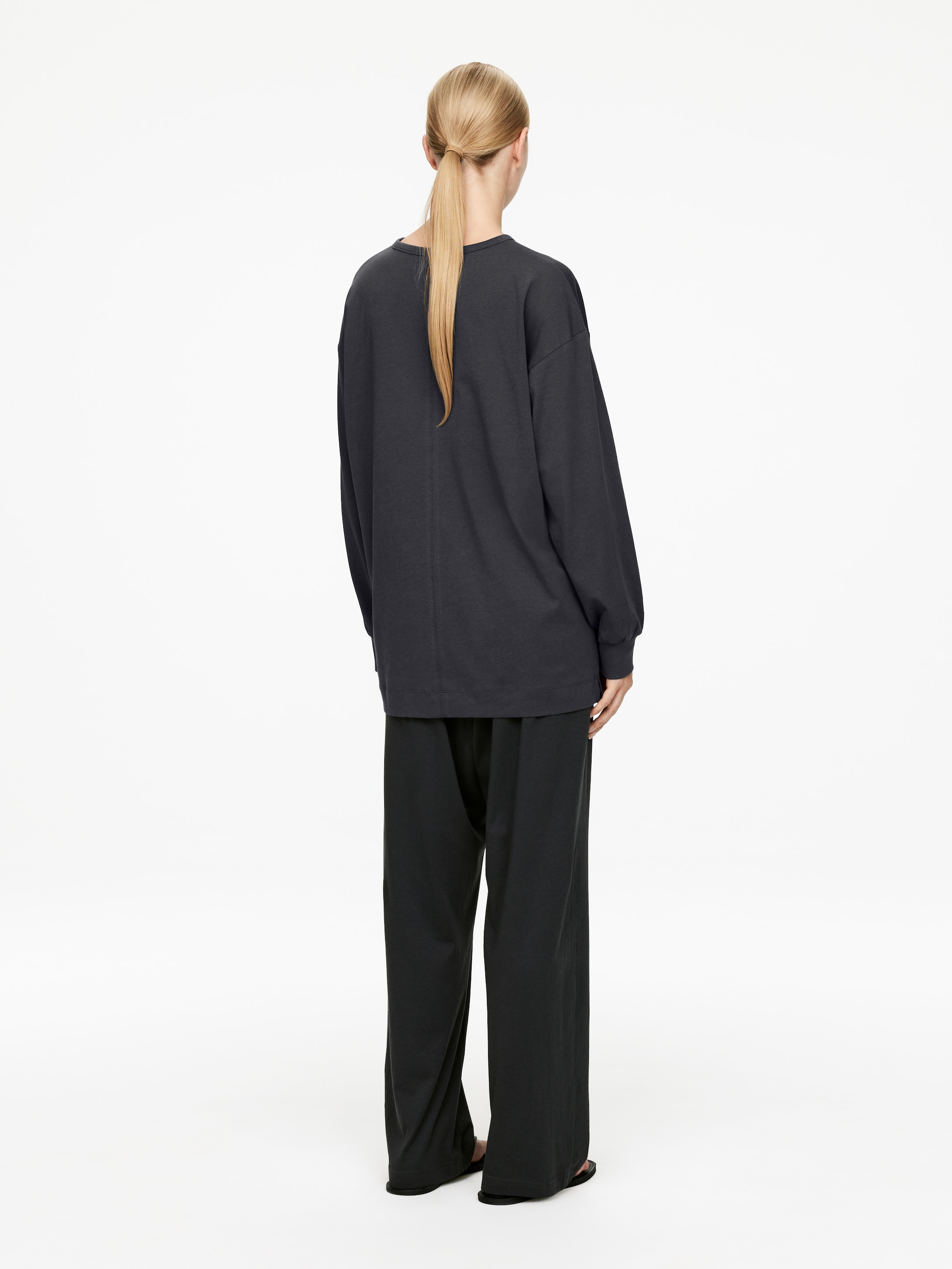 Agrandir l'image: Un haut à manches longues surdimensionné de couleur gris foncé est vu de dos, avec une couture verticale qui descend au centre. Il est associé à un pantalon large de couleur gris foncé assorti, les deux vêtements présentant une silhouette décontractée et fluide.